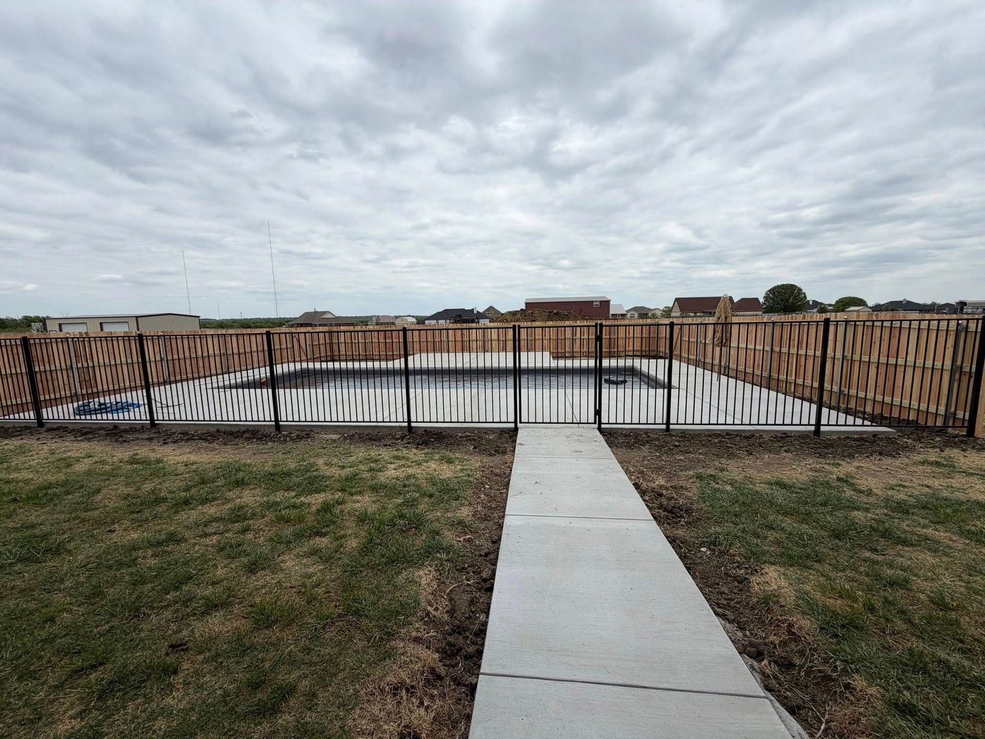 Concrete path to a fenced retaining wall under a cloudy sky, with grassy field in front