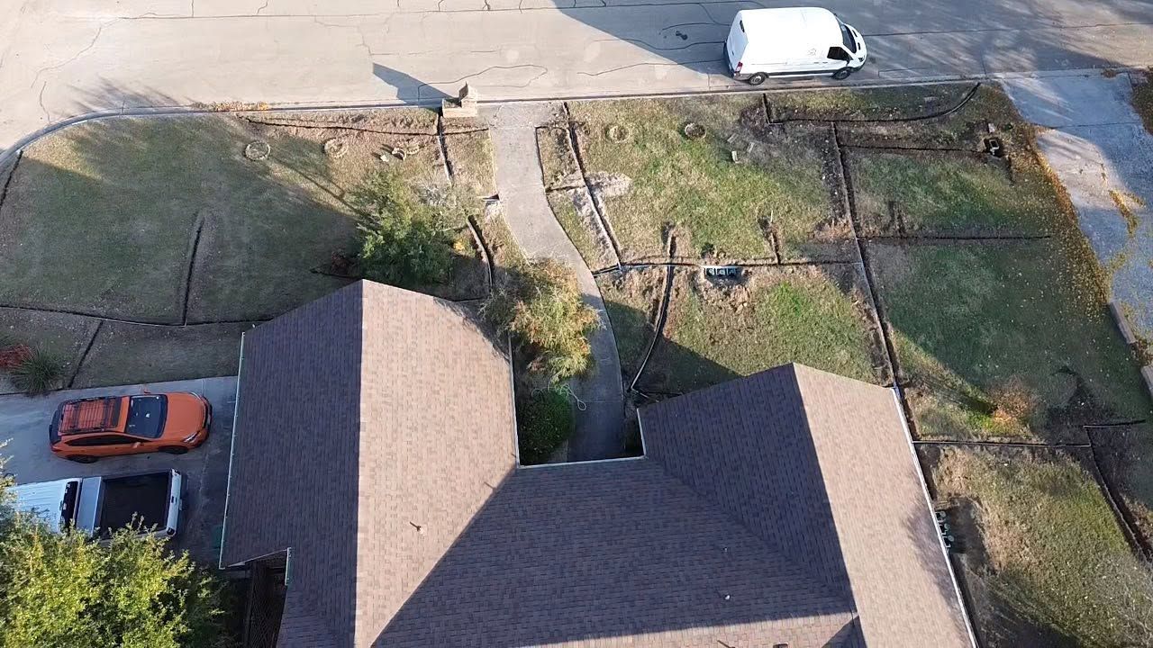 Aerial view of a residential yard with two parked cars, a sidewalk, and a house roof in the foreground.