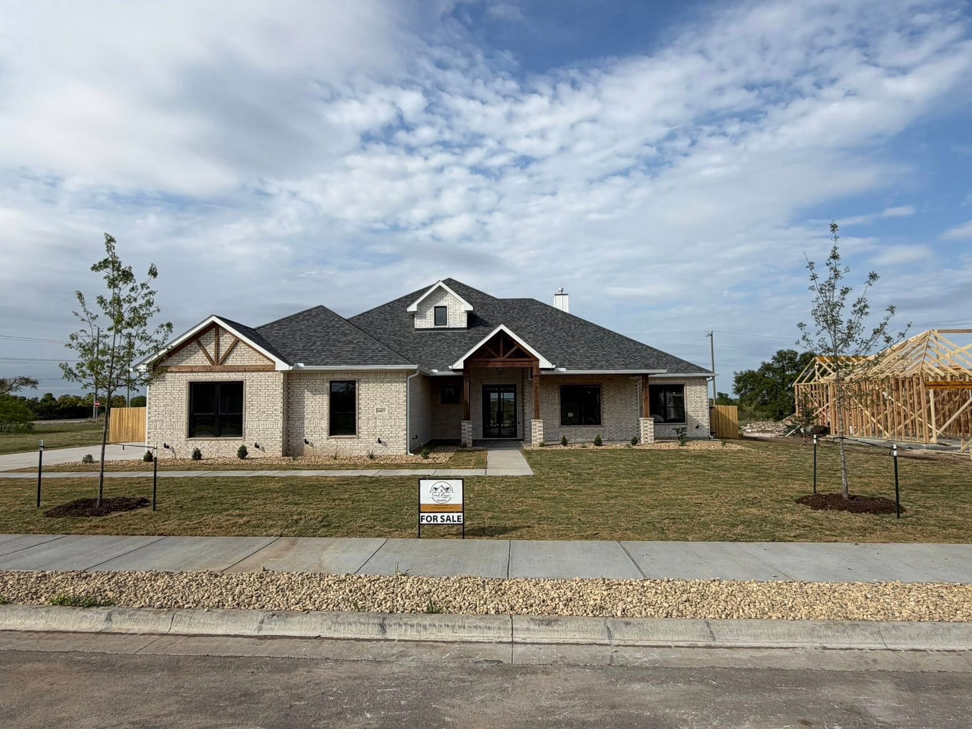 Single-story stone house under construction with a dark roof and unfinished front yard.