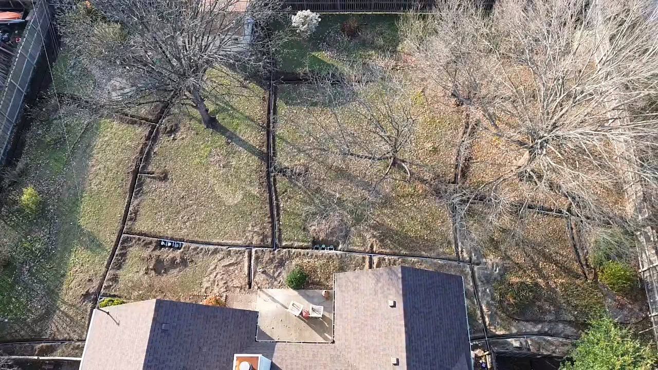 Aerial view of a backyard with leafless trees, grass, and two building roofs at the bottom edge