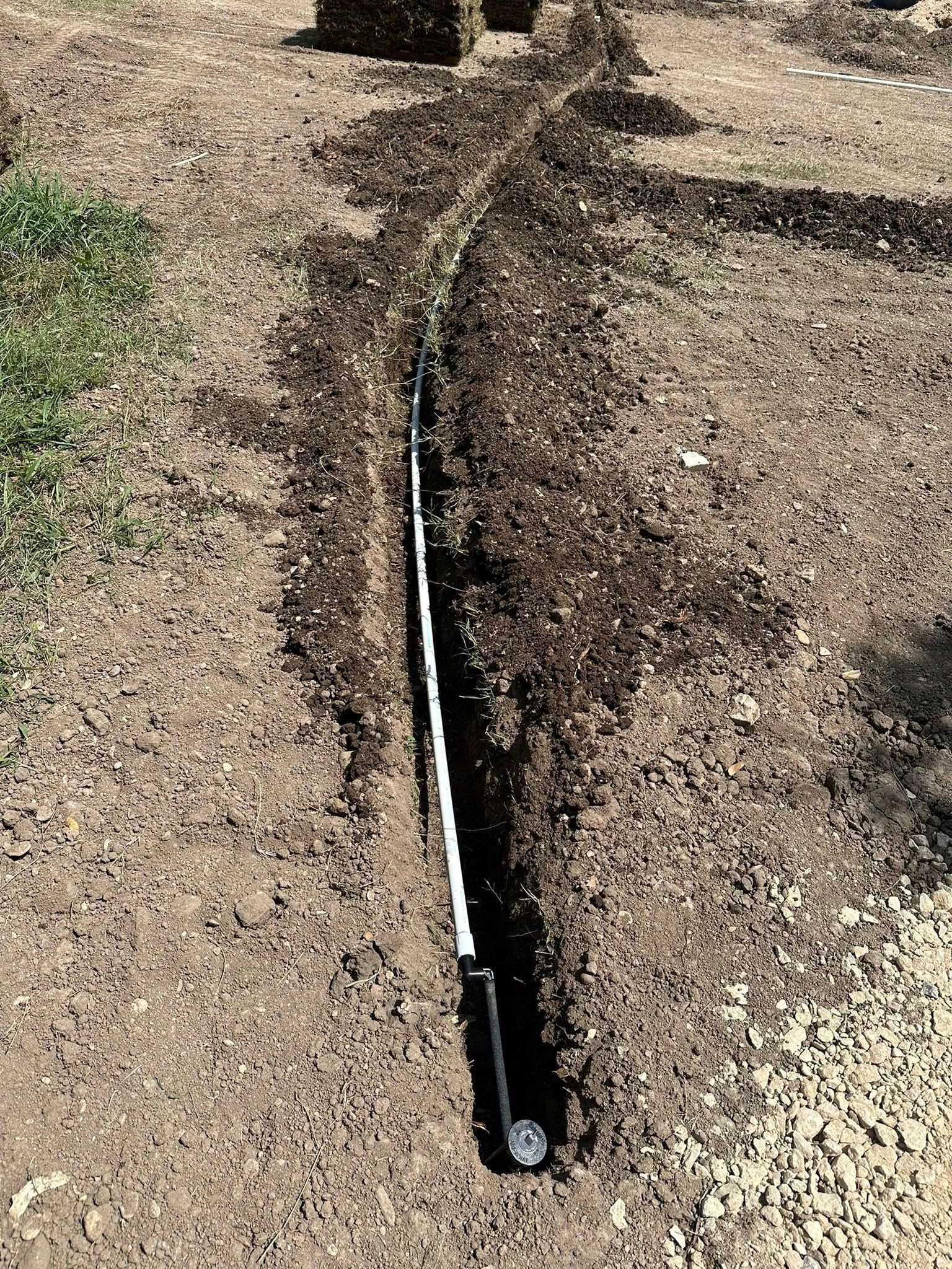 Black irrigation hose laid along a dirt and gravel path outdoors.