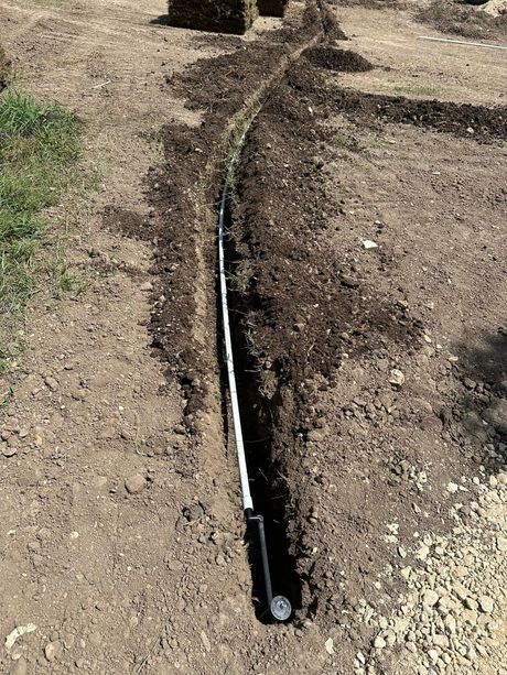 Black irrigation hose laid along a dirt and gravel path outdoors.