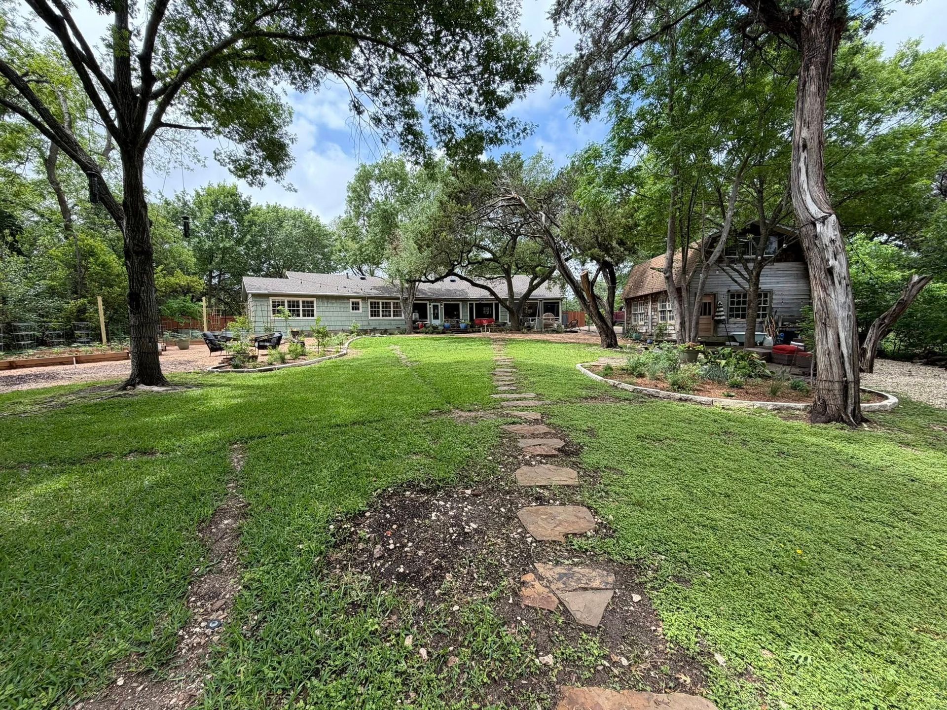 Tree-lined yard with stone path leading to a single-story house on a sunny day