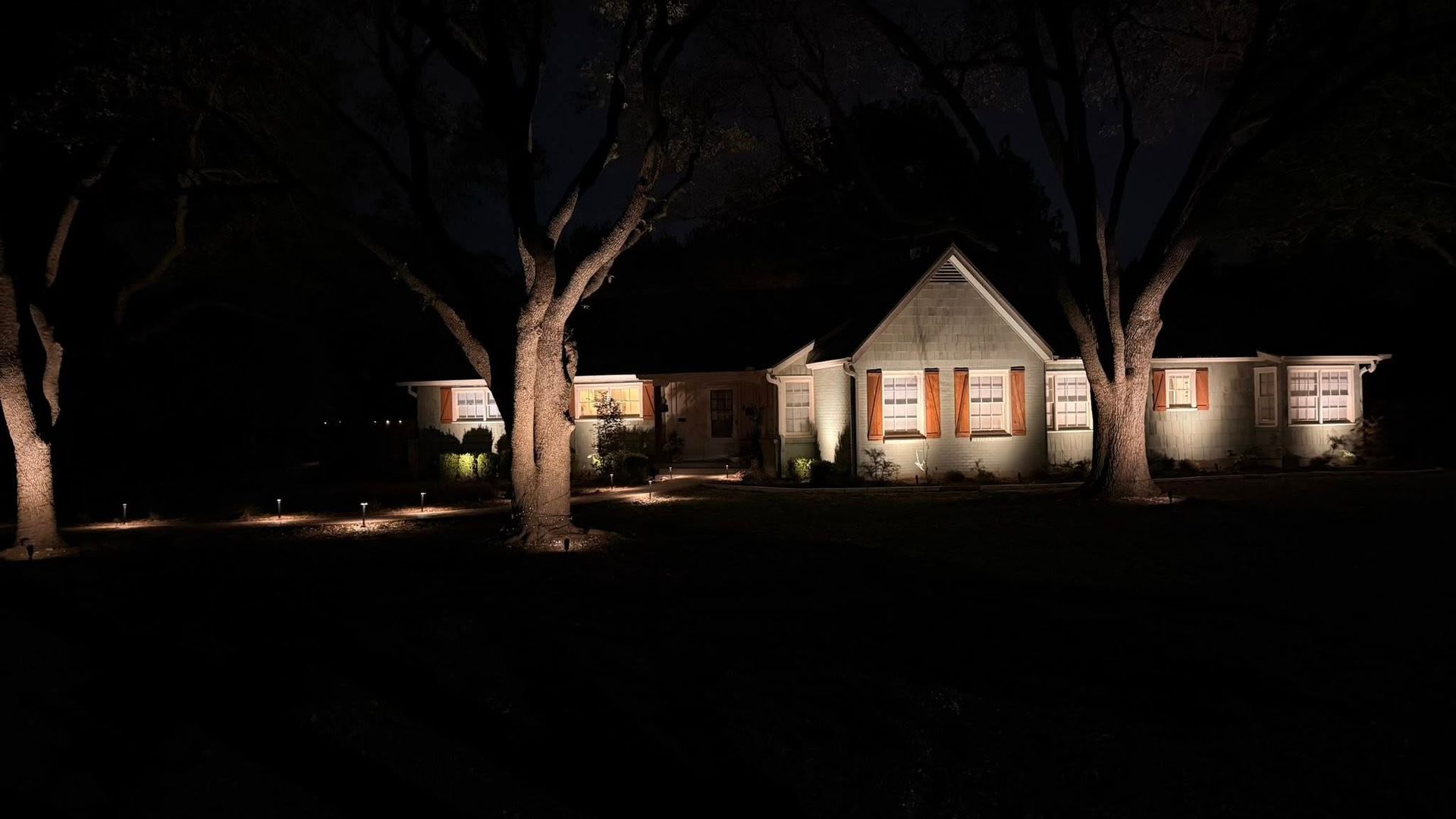 House lit at night with warm porch lights and large trees in the yard
