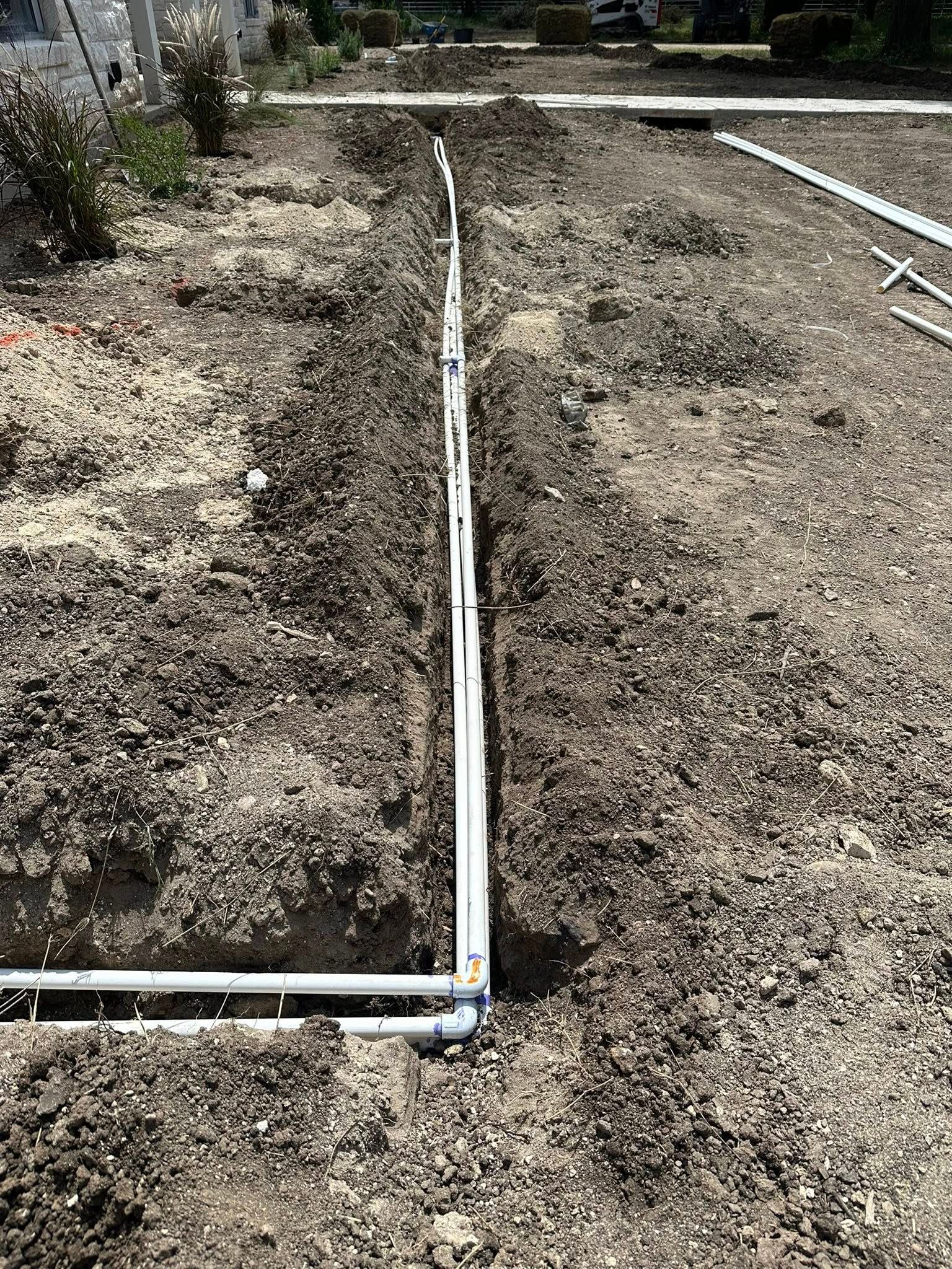Narrow white pipe trench running through a dry dirt field at a construction site