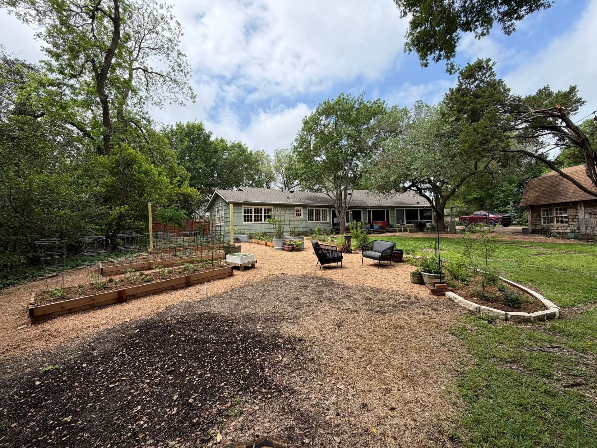 Spacious backyard garden with gravel paths, raised beds, trees, and a house in the background.