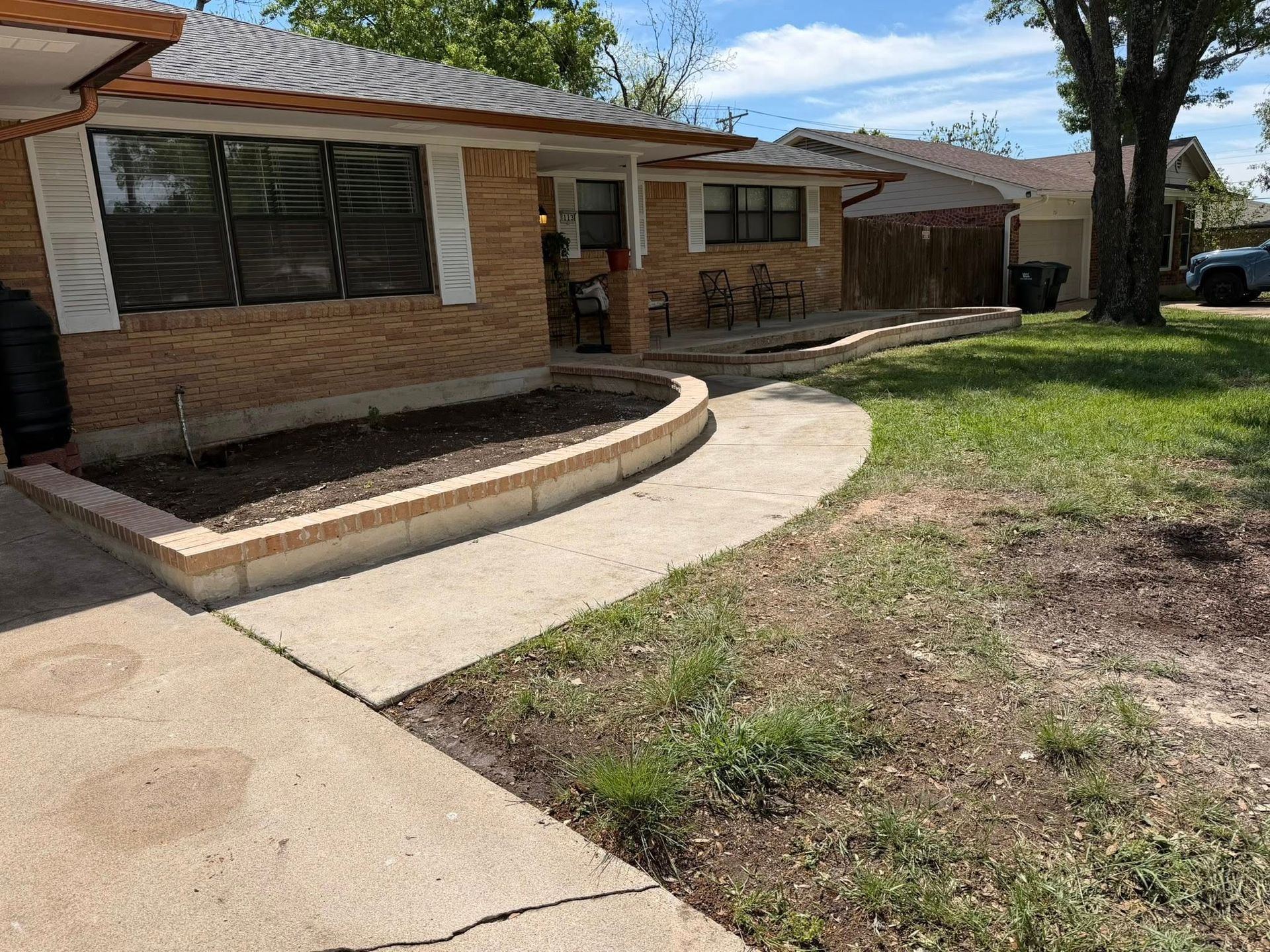Single-story brick house with a curved concrete walkway and grassy front yard under a sunny sky
