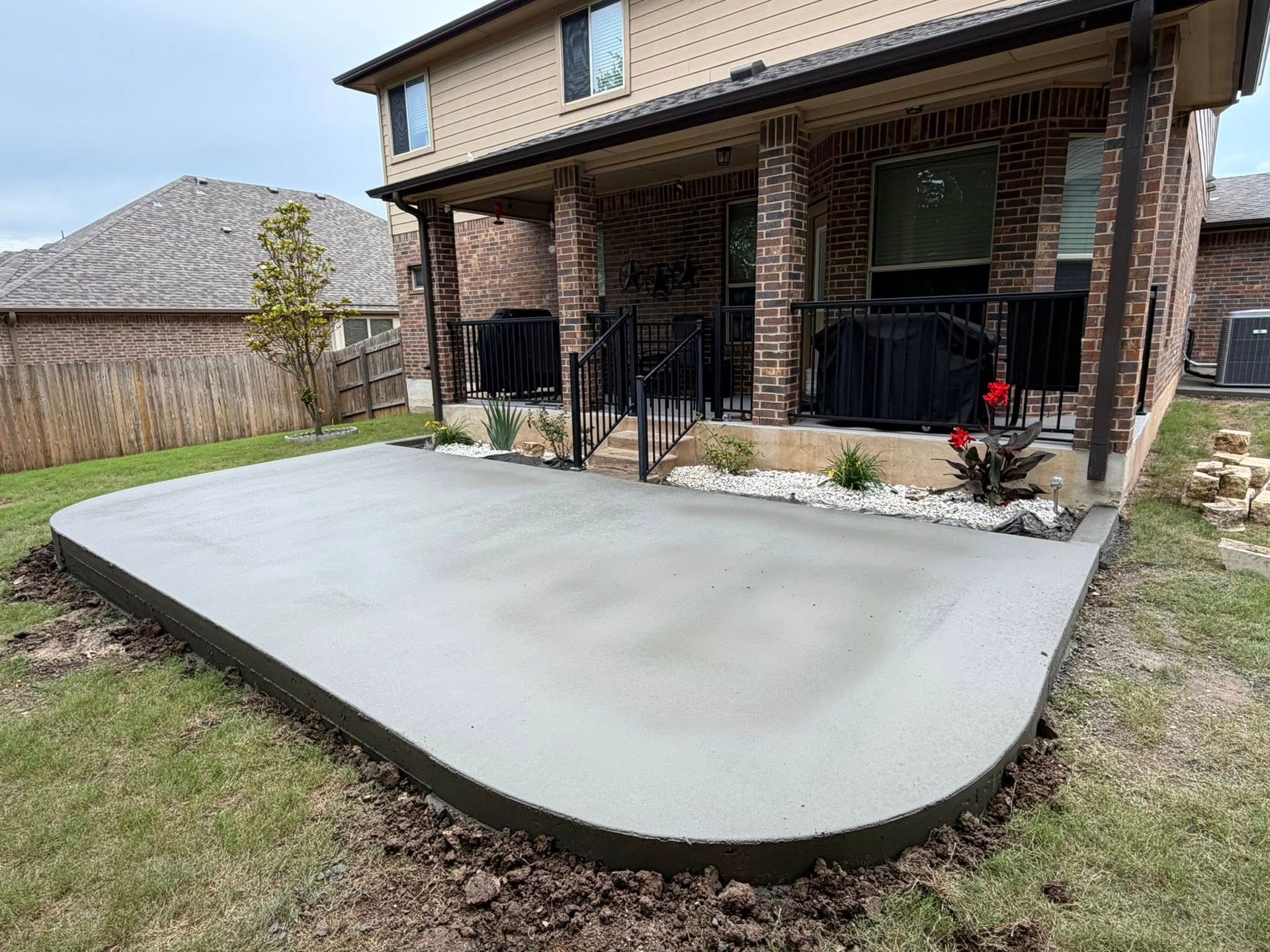 New concrete backyard patio slab beside a brick house with a curved front edge