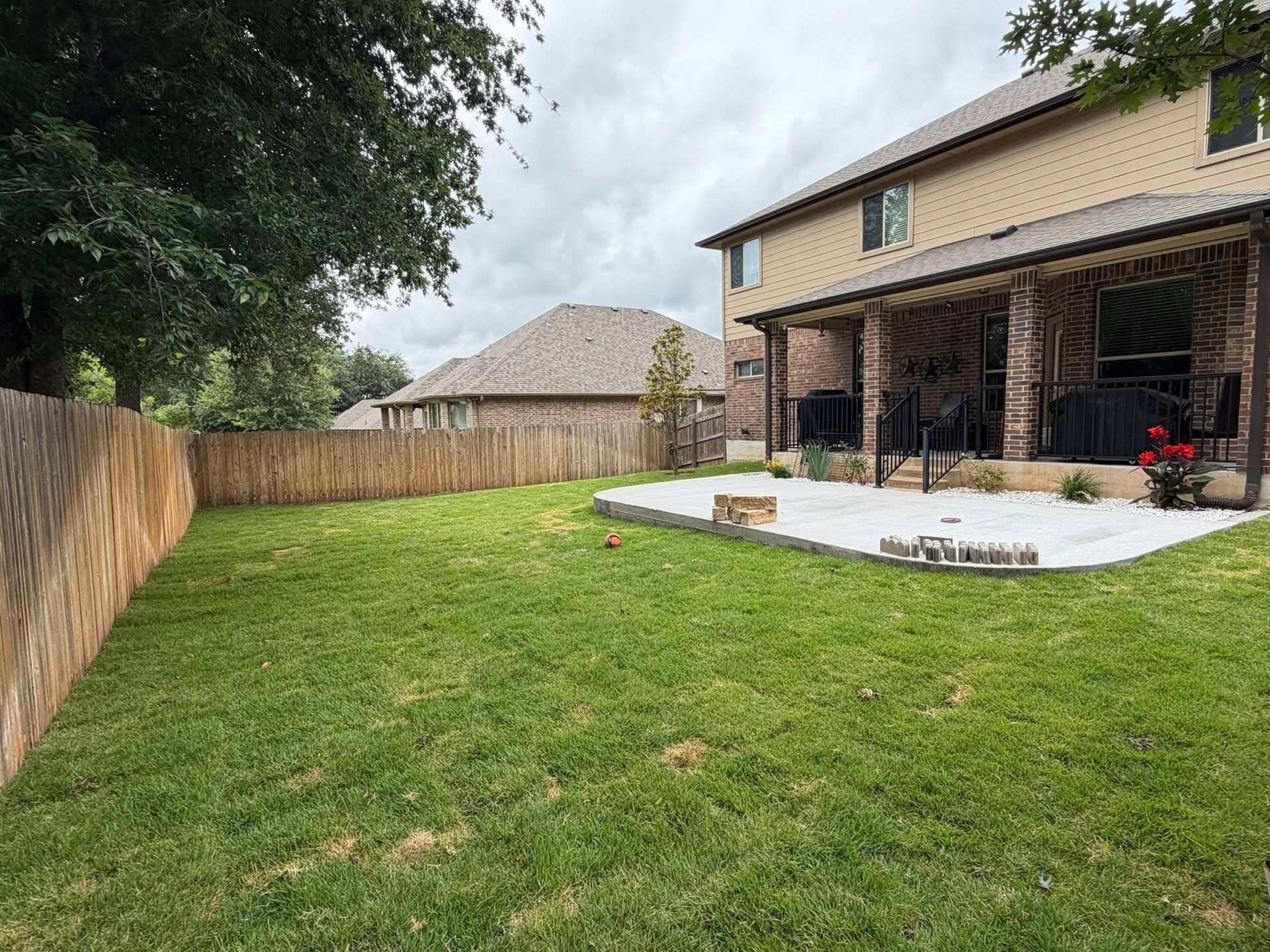 Backyard with green lawn, wooden fence, and covered patio beside a two-story house