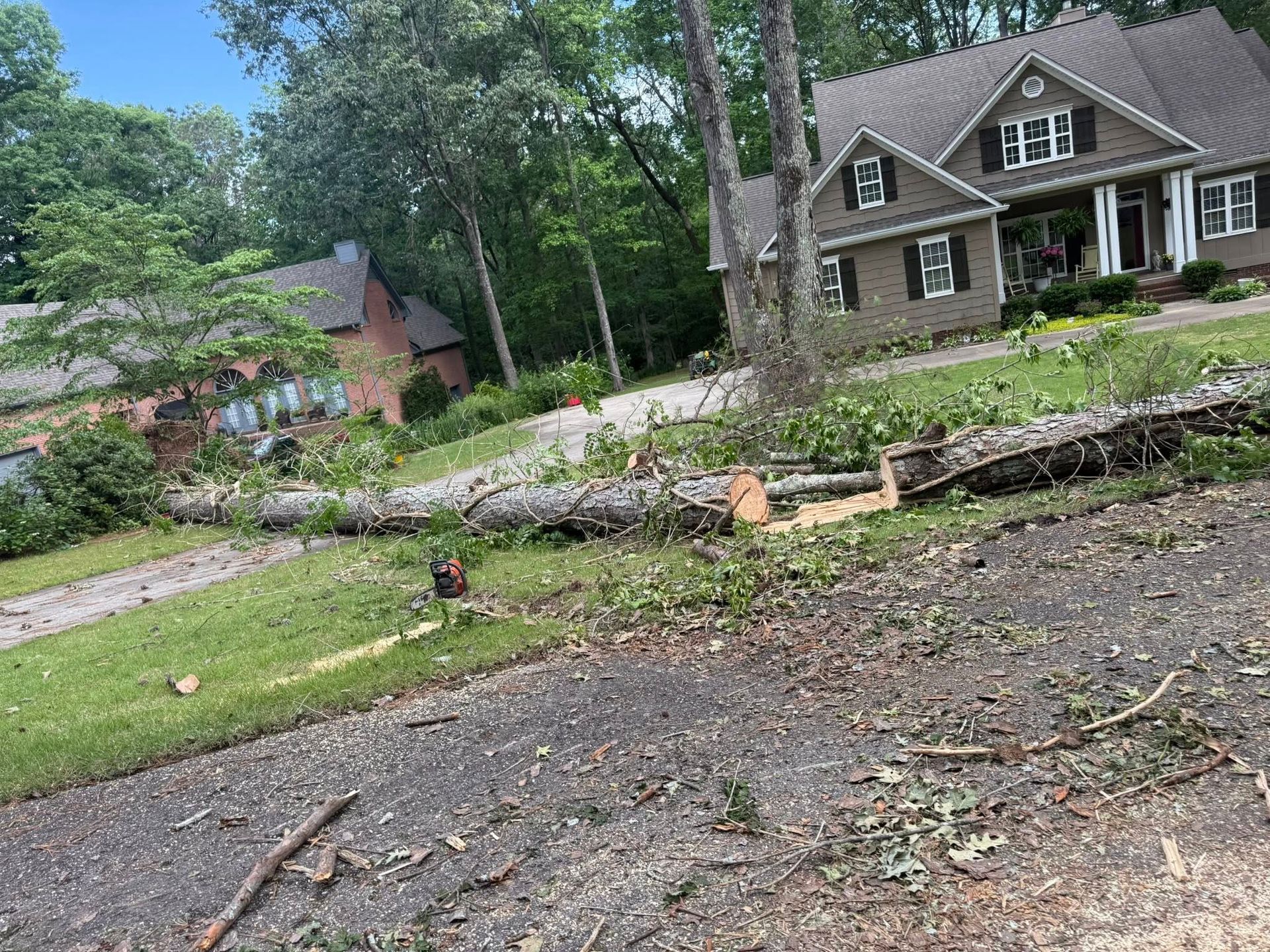 Storm-damaged yard with fallen tree limbs and debris in front of a suburban house