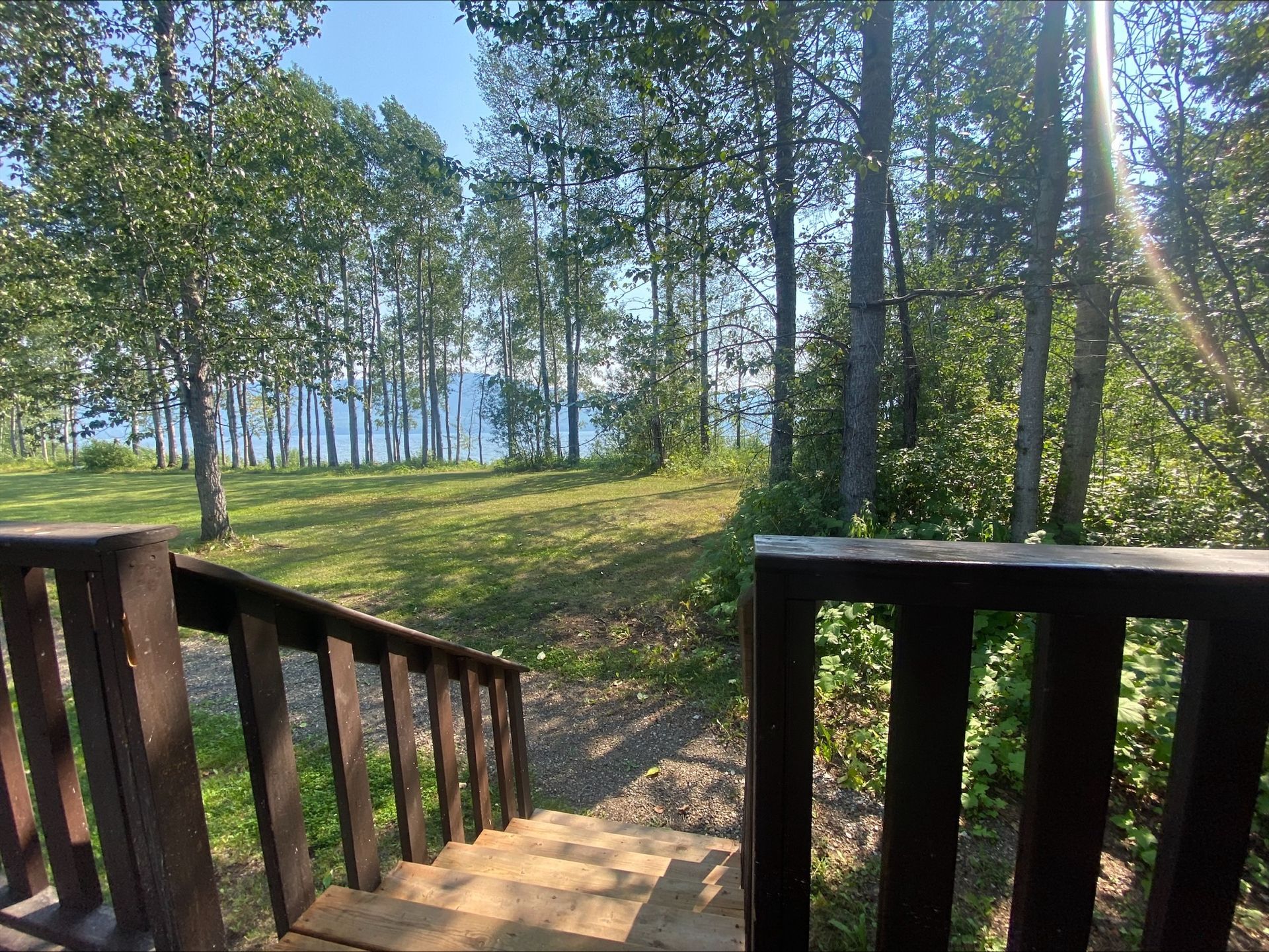A wooden deck with stairs leading up to a lake surrounded by trees.