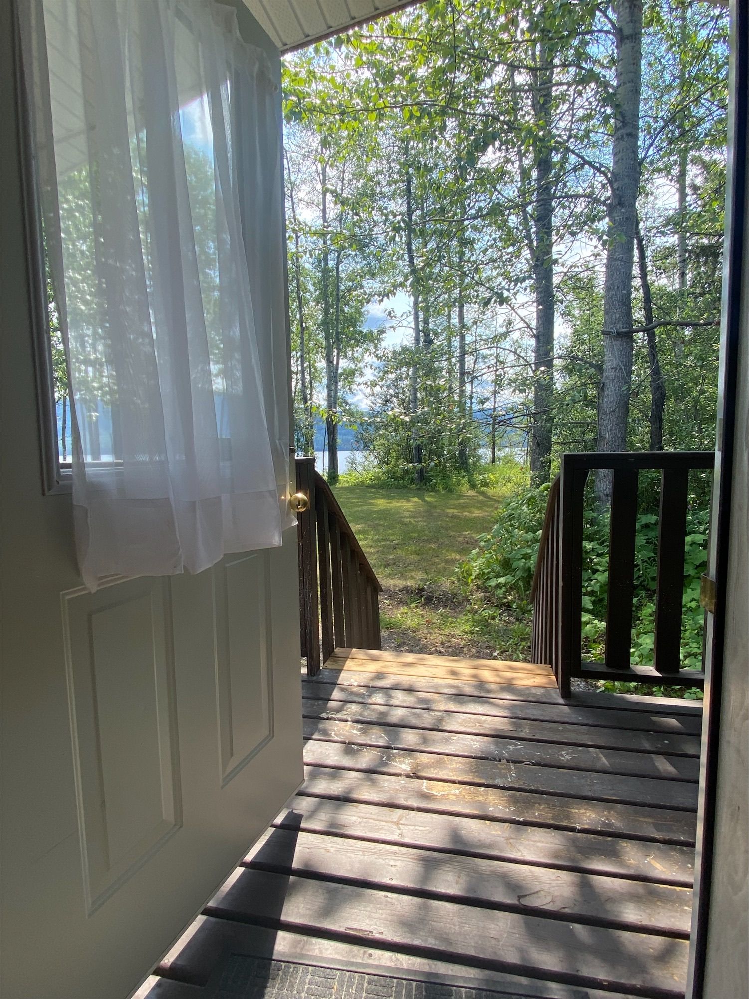 A doorway leading to a wooden deck with trees in the background.