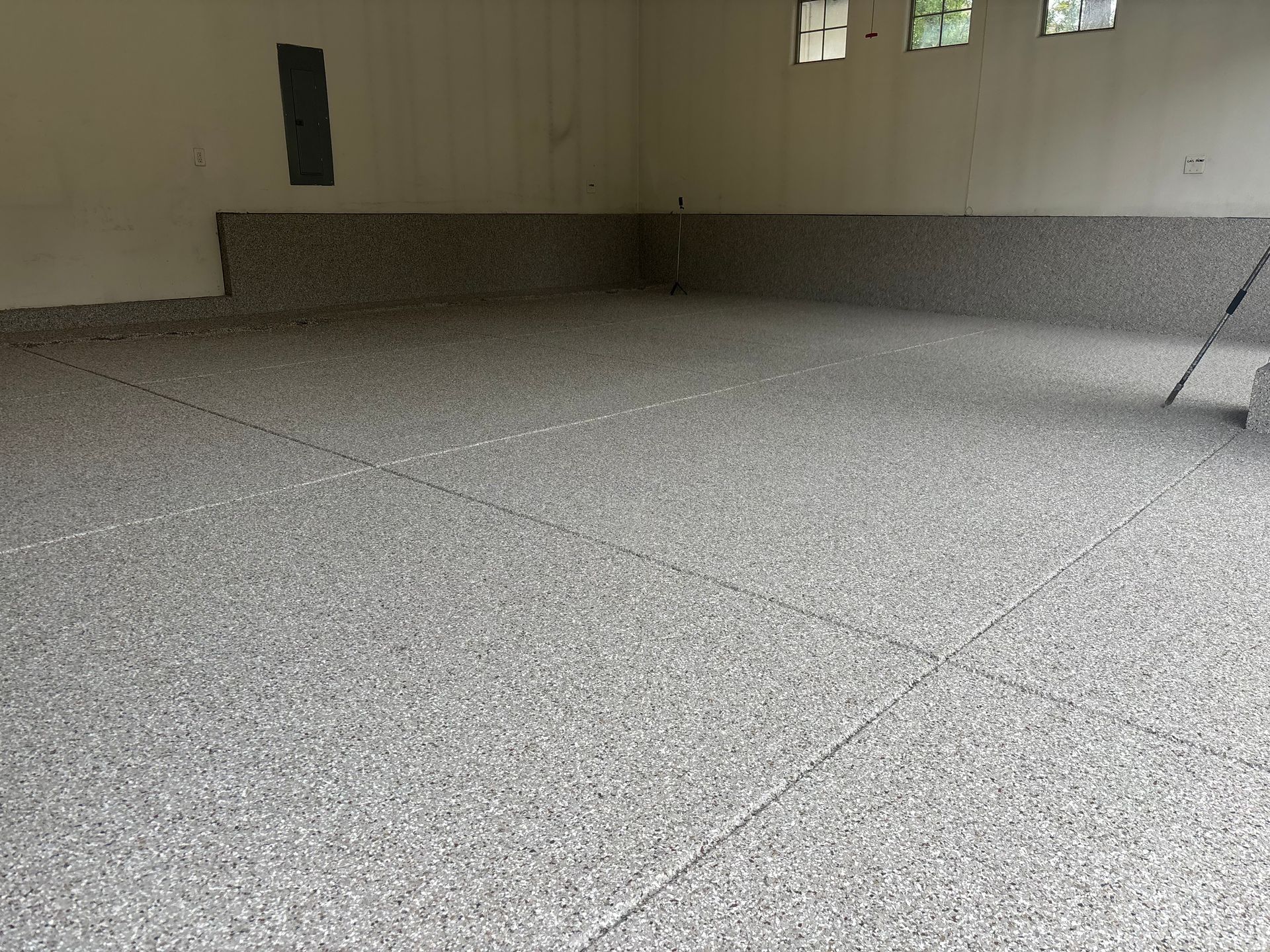 Large empty indoor room with beige walls and a speckled gray floor, viewed from a corner.