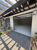 Covered driveway with white garage door, gray pavers, and black pergola beams casting shadows