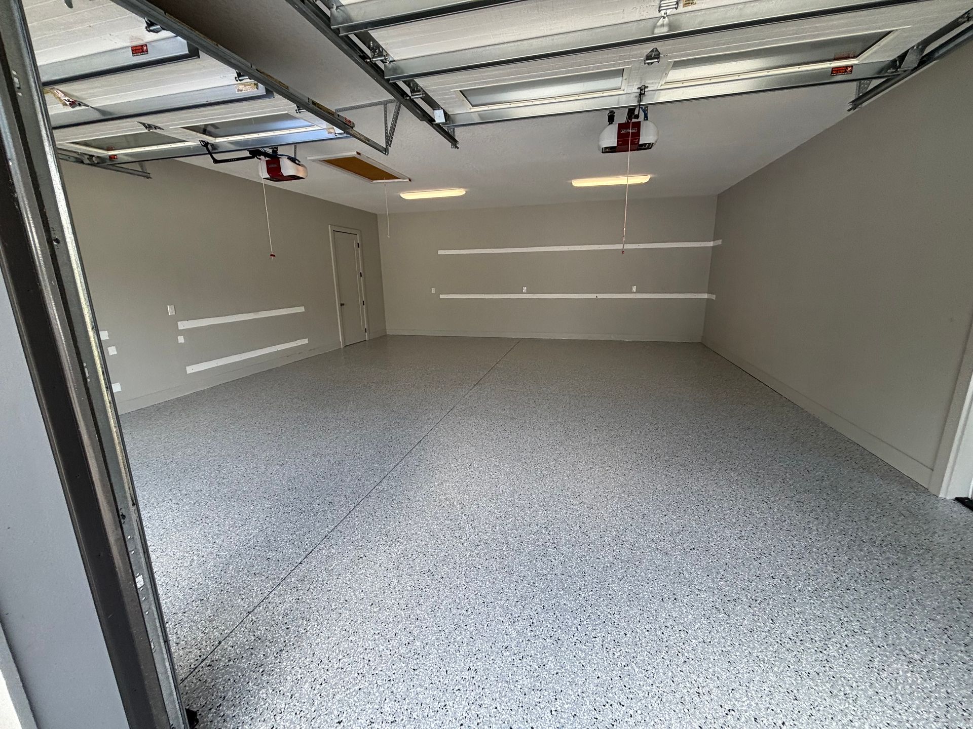 Empty beige garage with speckled floor and overhead door open