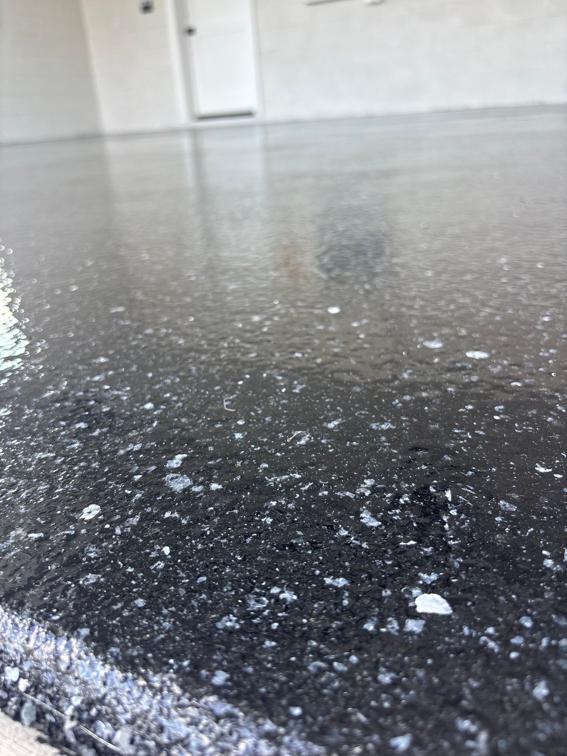 Close-up of a speckled black floor in an empty room with white walls and a door in the background