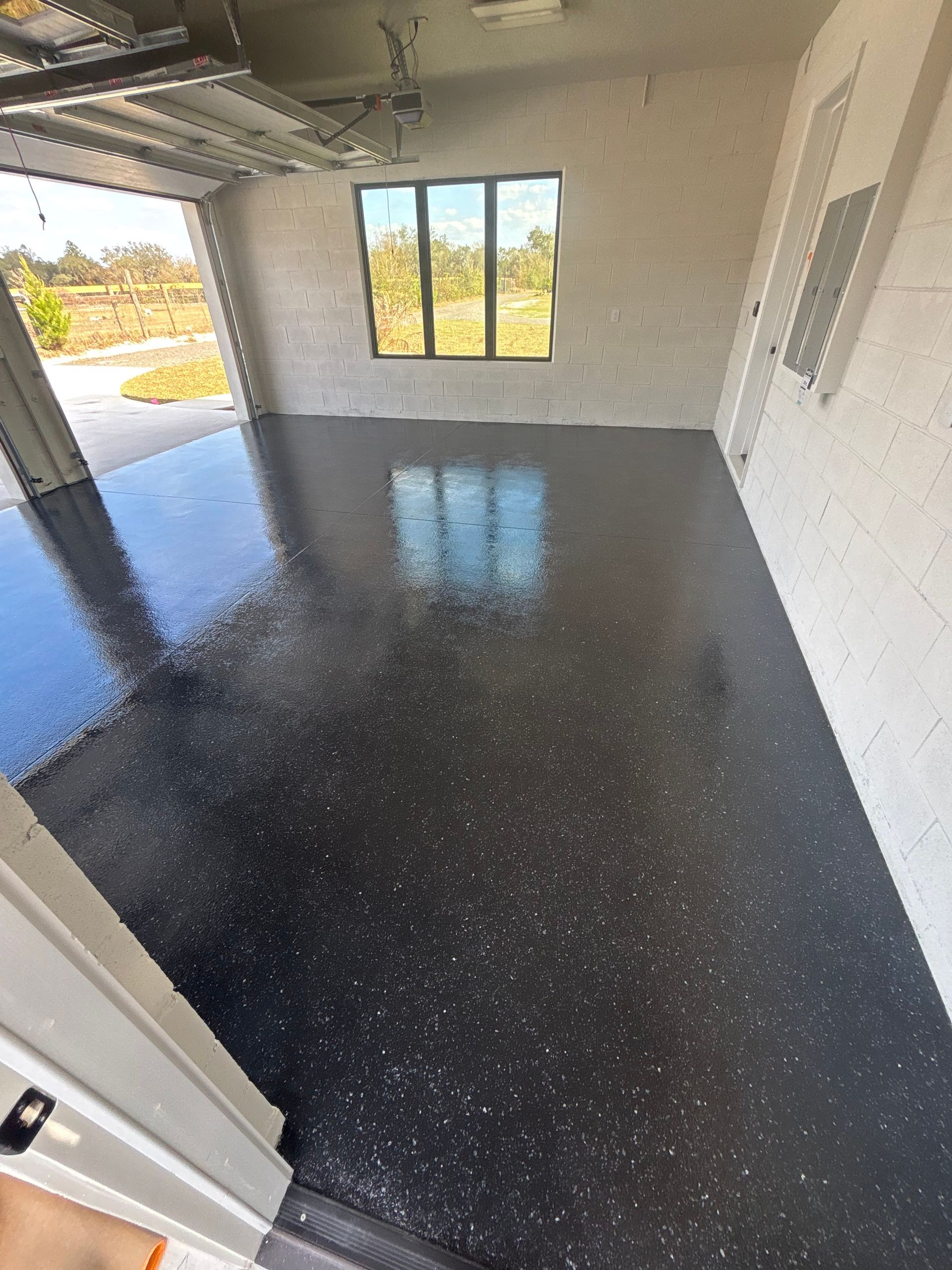 Empty covered patio with glossy black floor, white walls, and a window overlooking outside.