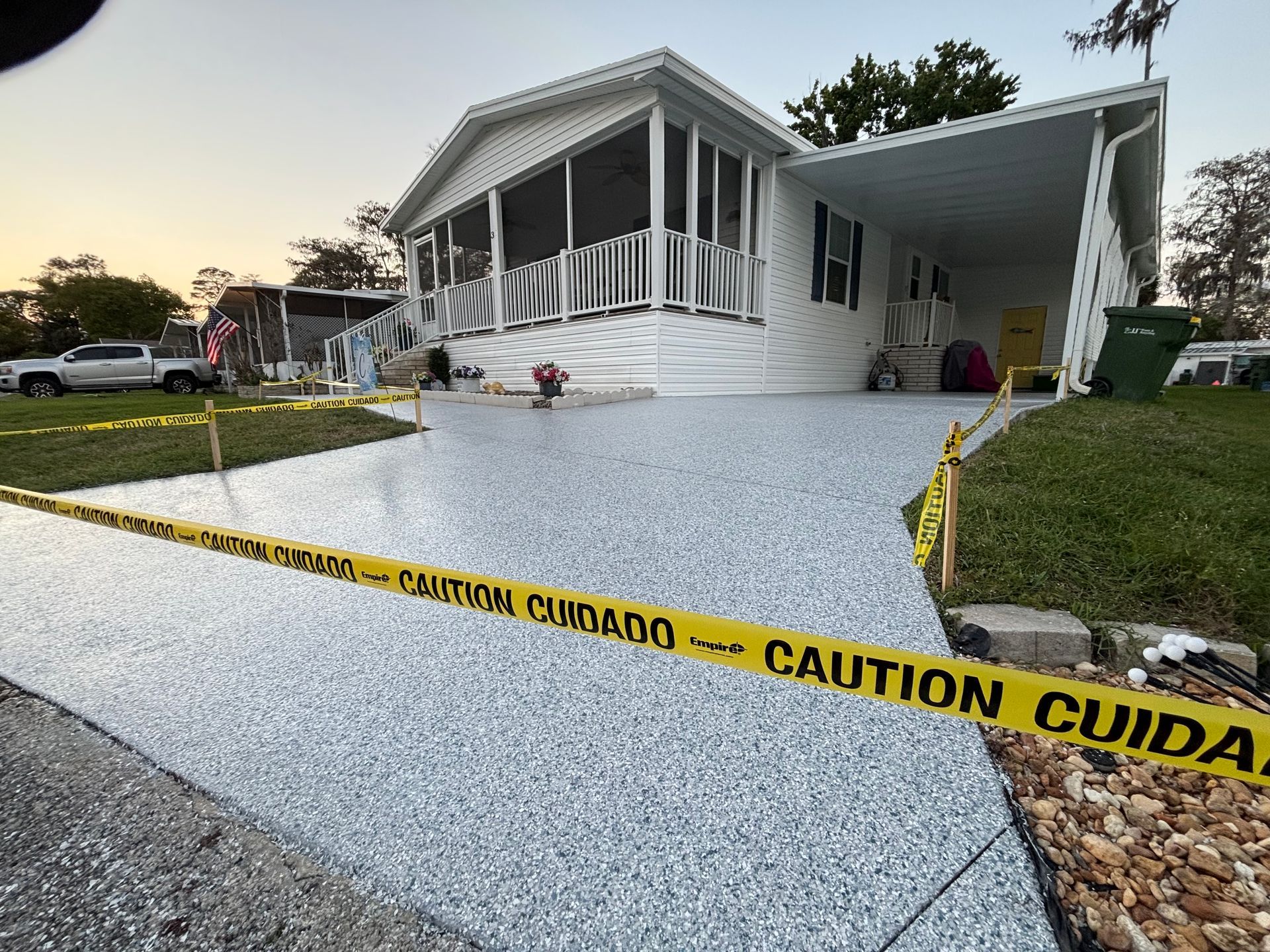 Caution tape blocks a freshly paved walkway leading to a white house on a rainy day.