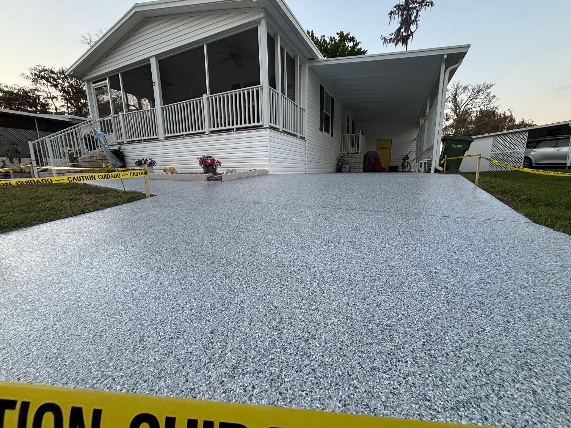 White textured driveway leading to a white house with porch and carport at dusk