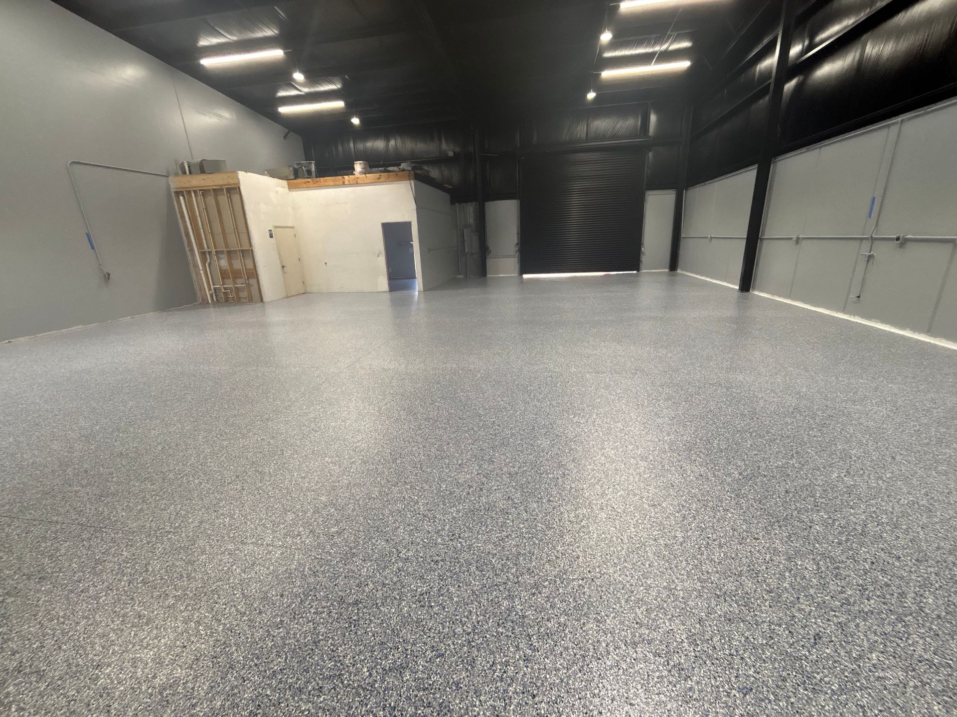 Empty industrial warehouse with gray epoxy floor, metal walls, and a small white office structure.