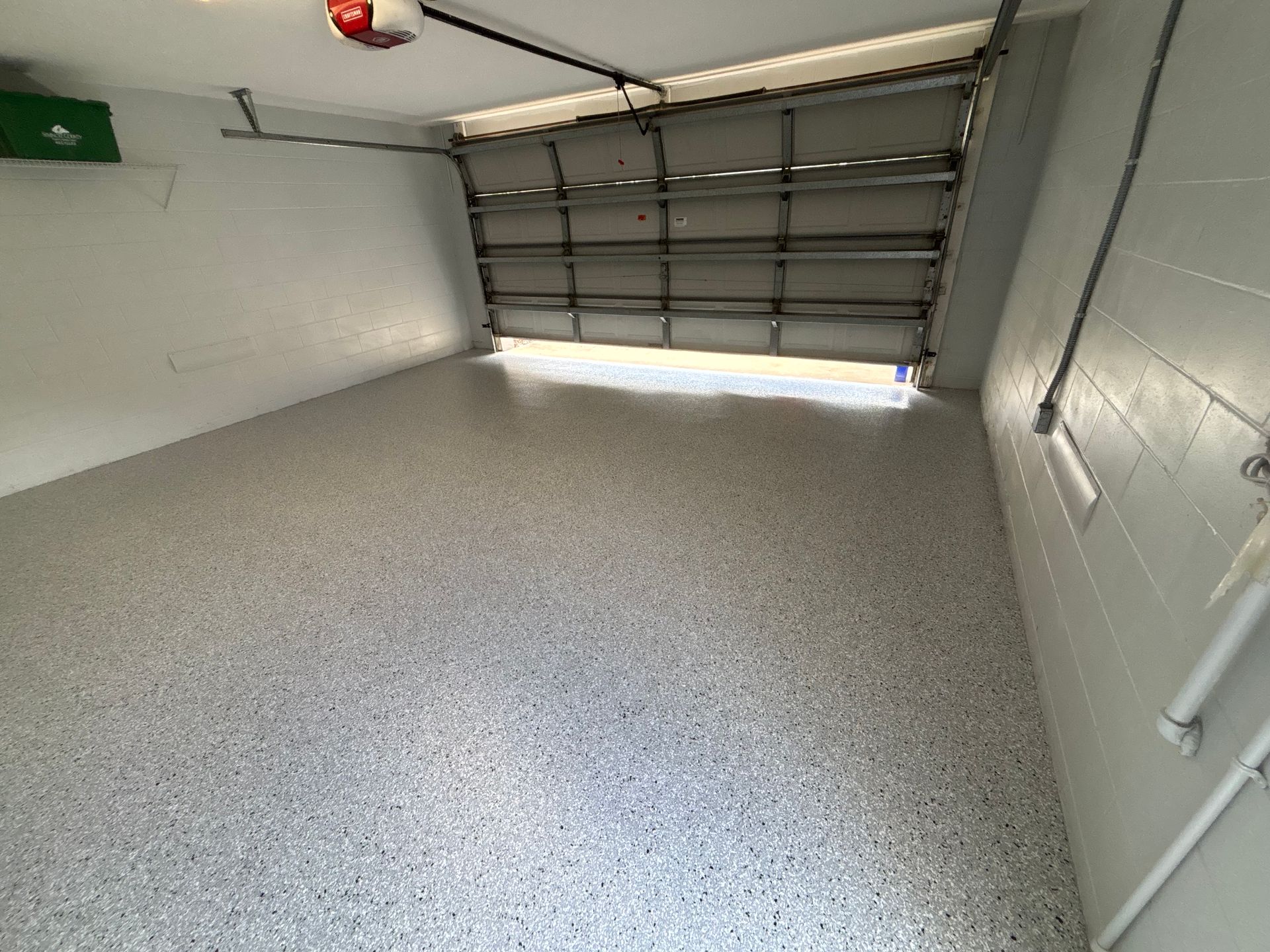 Empty garage with a closed door and speckled gray floor, lit by daylight.