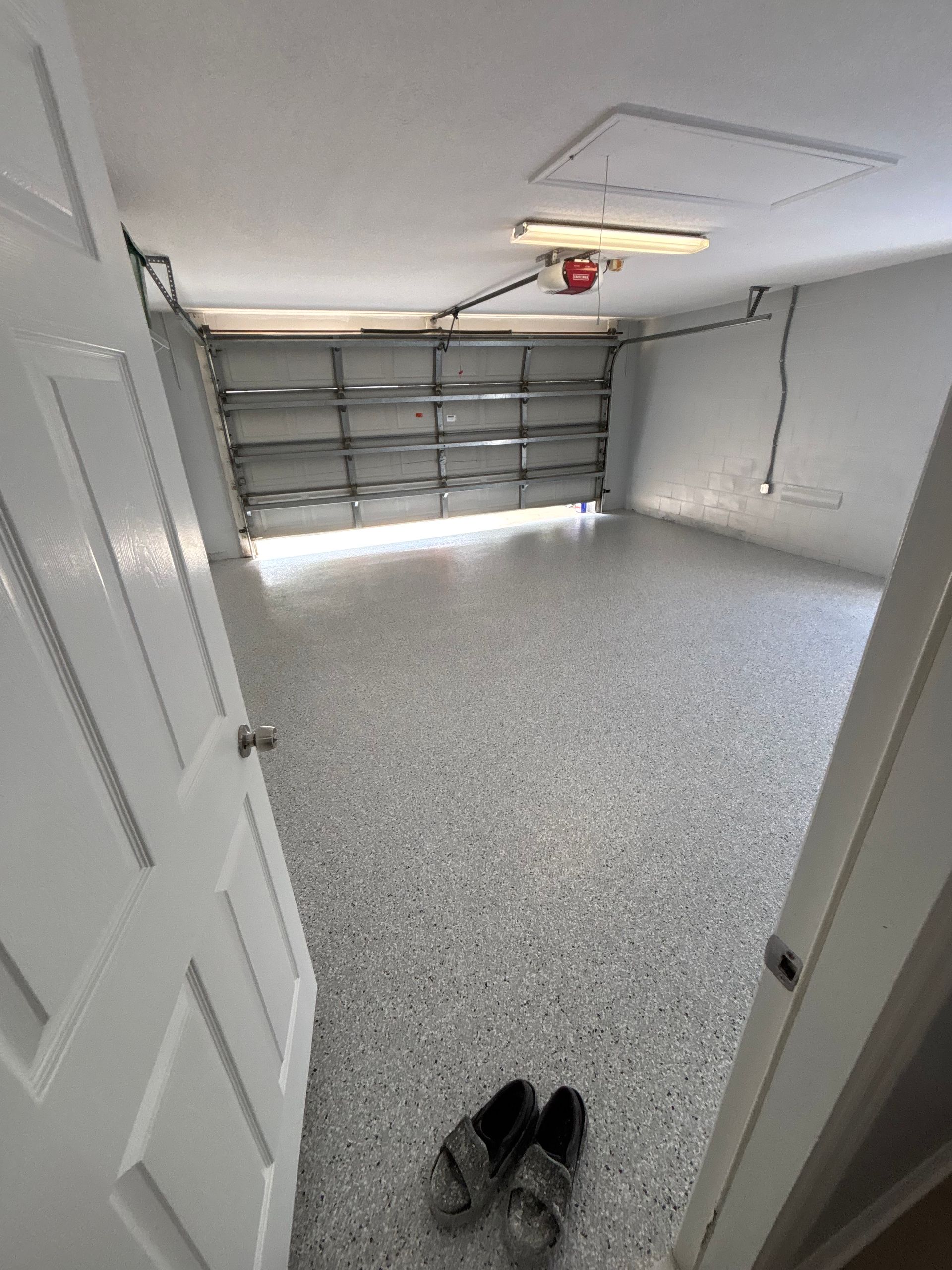 Open garage with speckled floor, closed garage door, and a pair of shoes near the entrance.