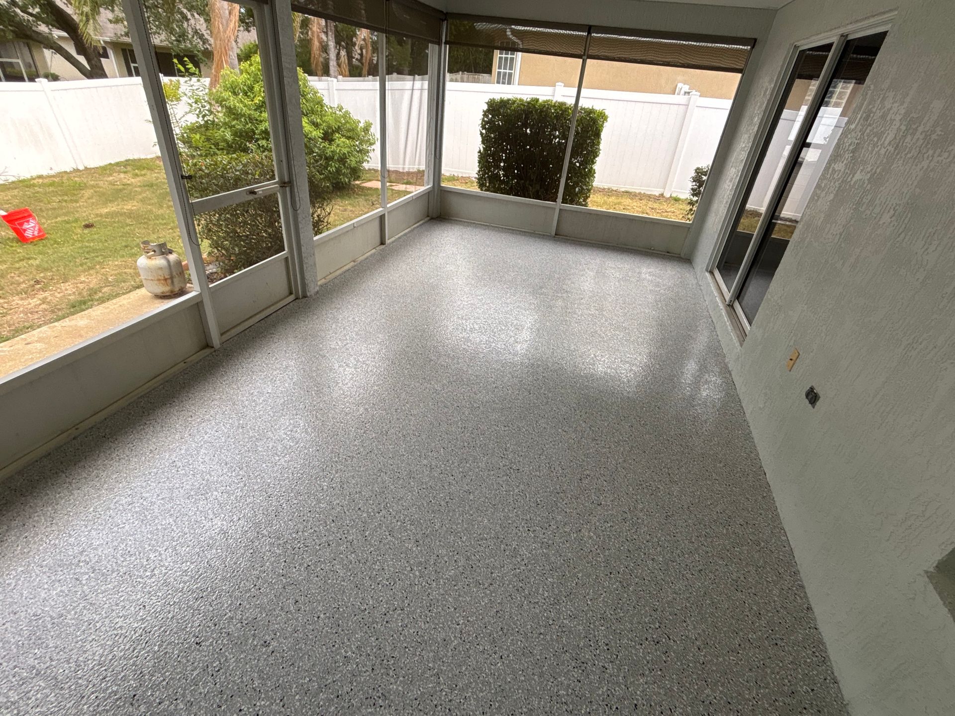 Covered patio with gray speckled floor, screened walls, and a view of the yard.