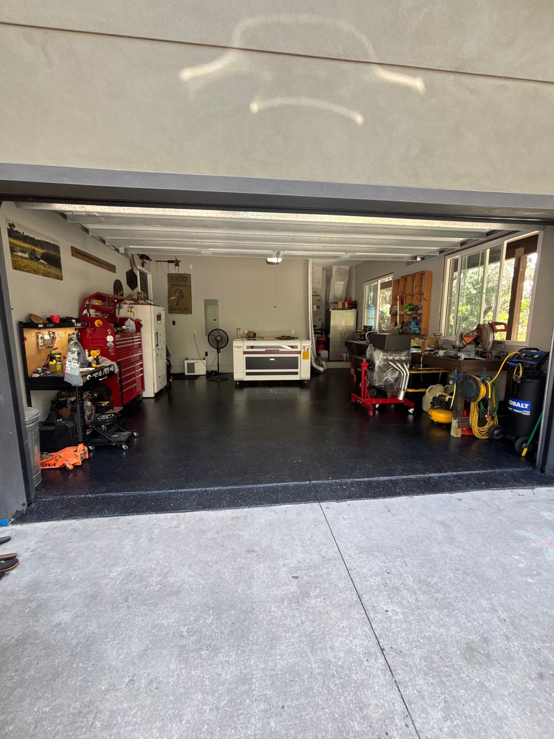 Open garage with a white car, red tool storage, and various equipment along the walls.