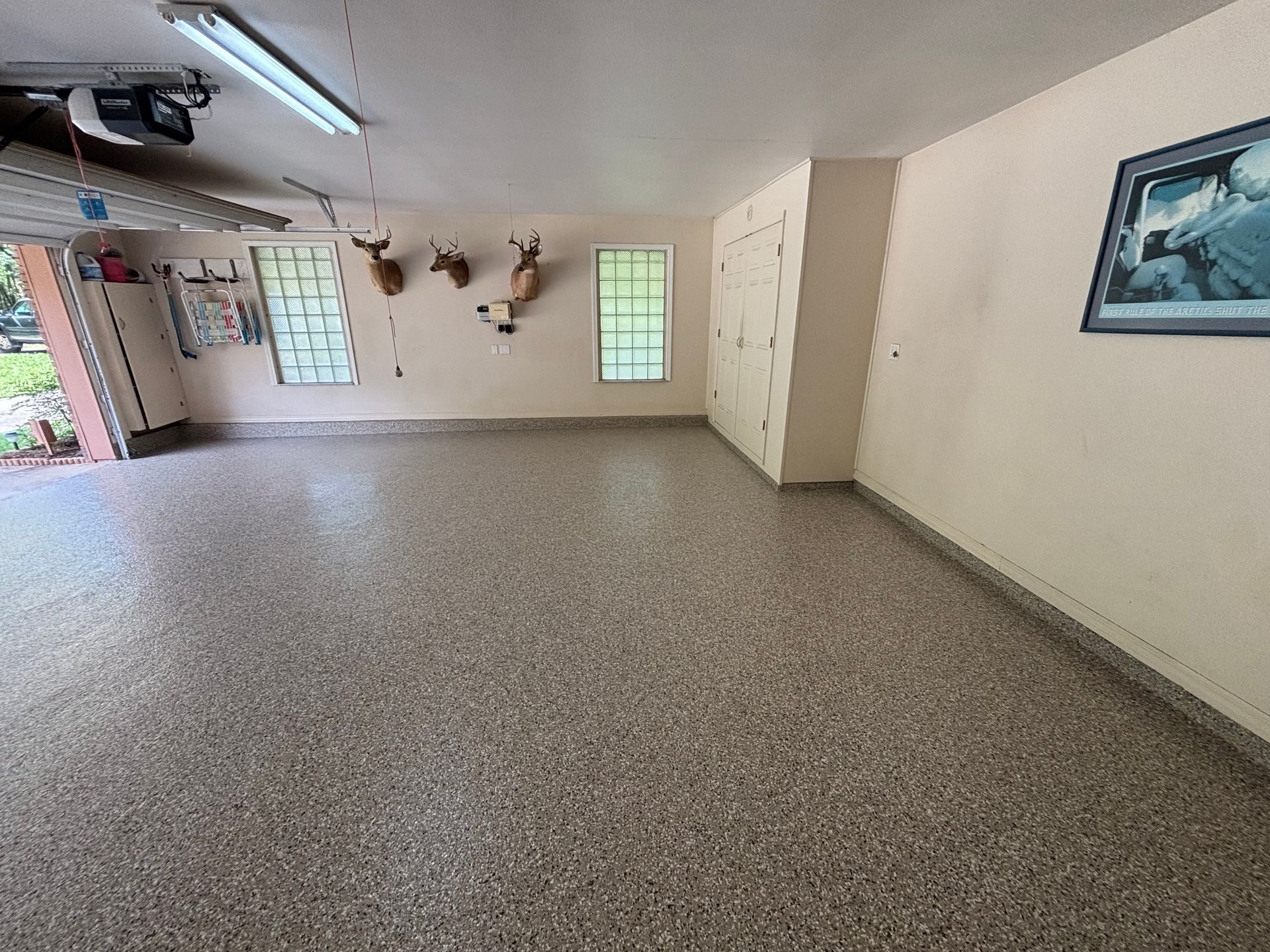 Empty speckled-floor room with mounted deer heads, windows, and a framed painting on the wall