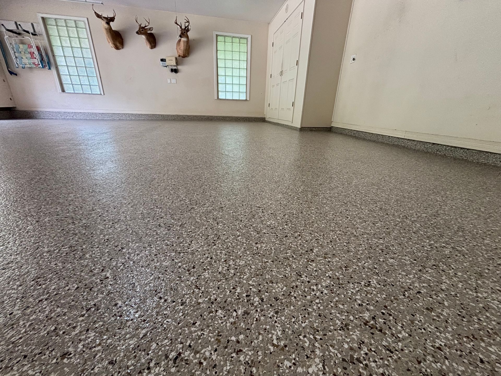 Empty room with speckled epoxy floor, white walls, windows, and mounted deer heads on the far wall