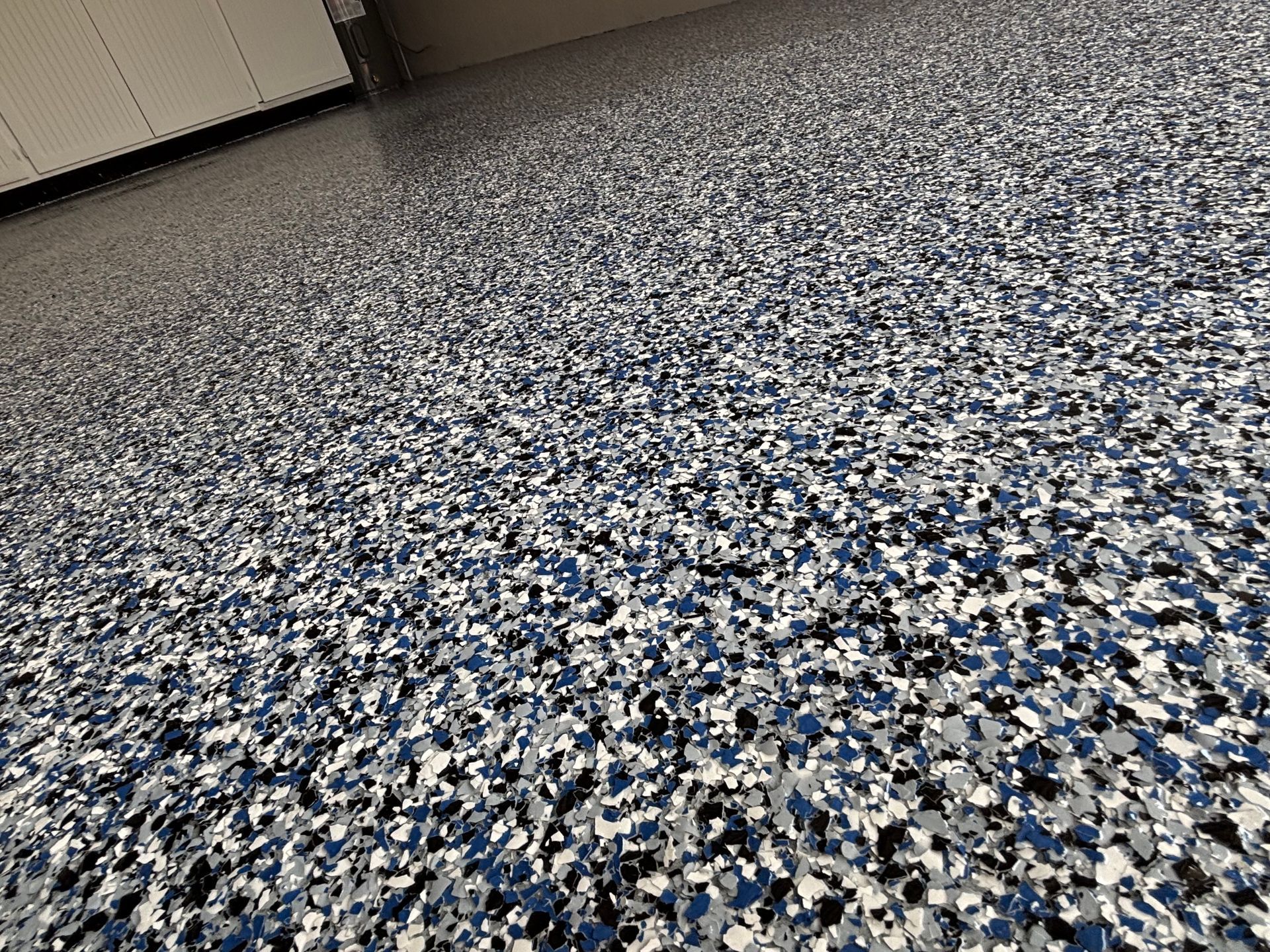 Blue, white, and gray speckled epoxy floor in an empty indoor room, seen at an angle.