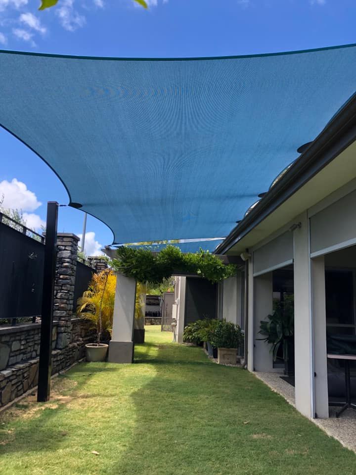 A large blue shade sail is hanging over a lush green yard.