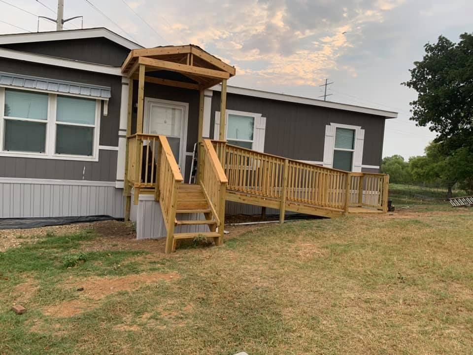 A wooden wheelchair ramp and steps with a covered porch leading to the front door of a gray manufactured home.