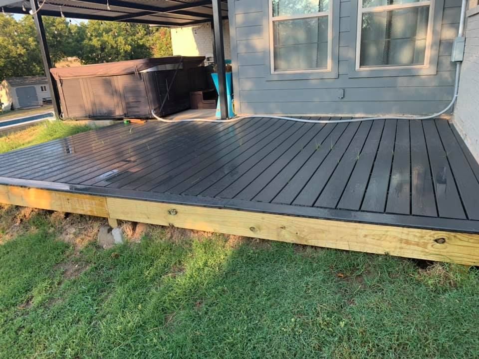 A dark gray wooden deck with an unfinished light wood frame, situated next to a hot tub and the side of a house.