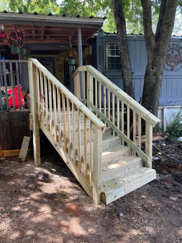 Newly constructed wooden staircase with handrails leading to an elevated porch entrance outdoors.