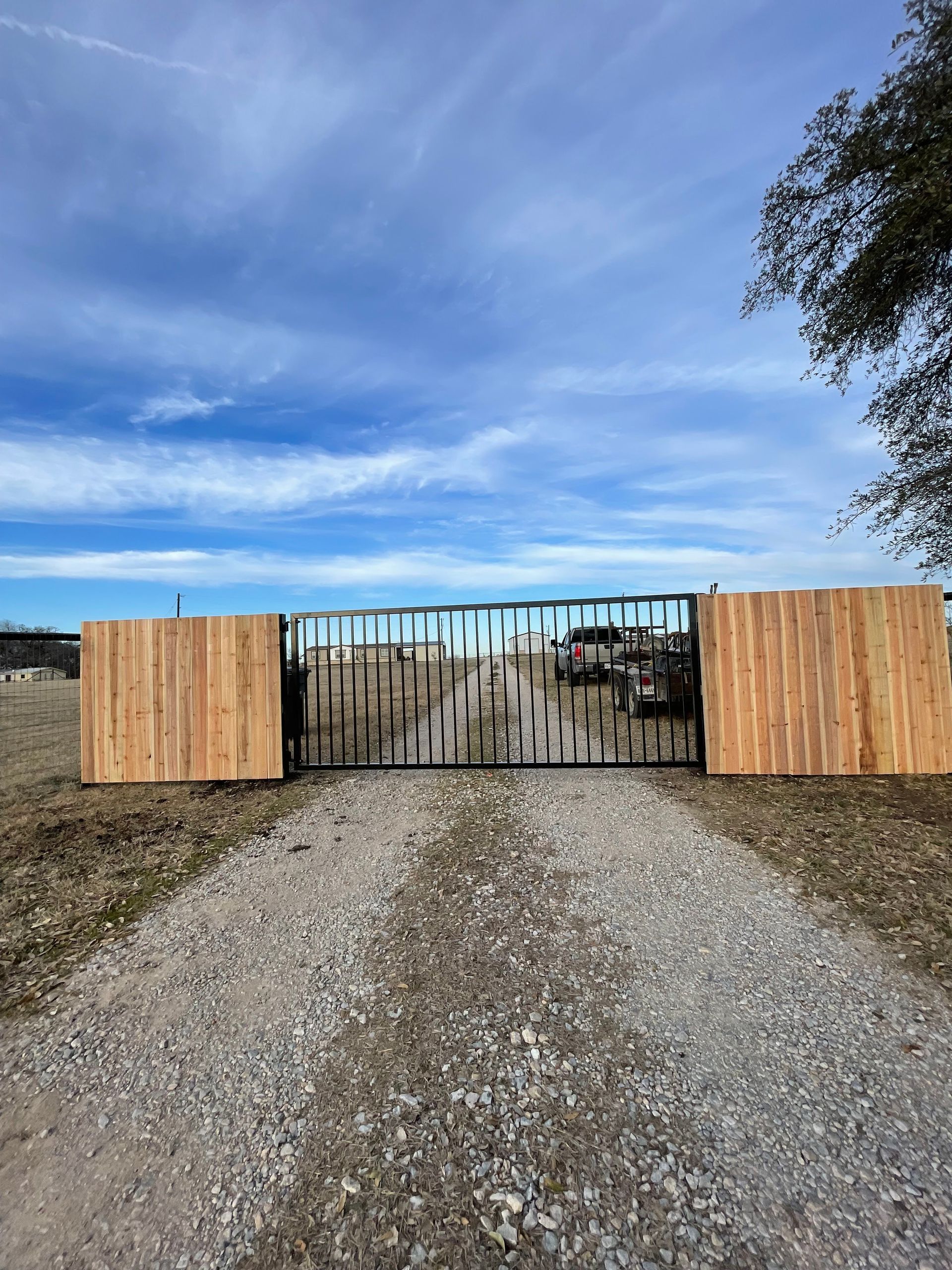 A metal gate with vertical spikes stands between two wooden panels on a gravel path under a bright blue sky.