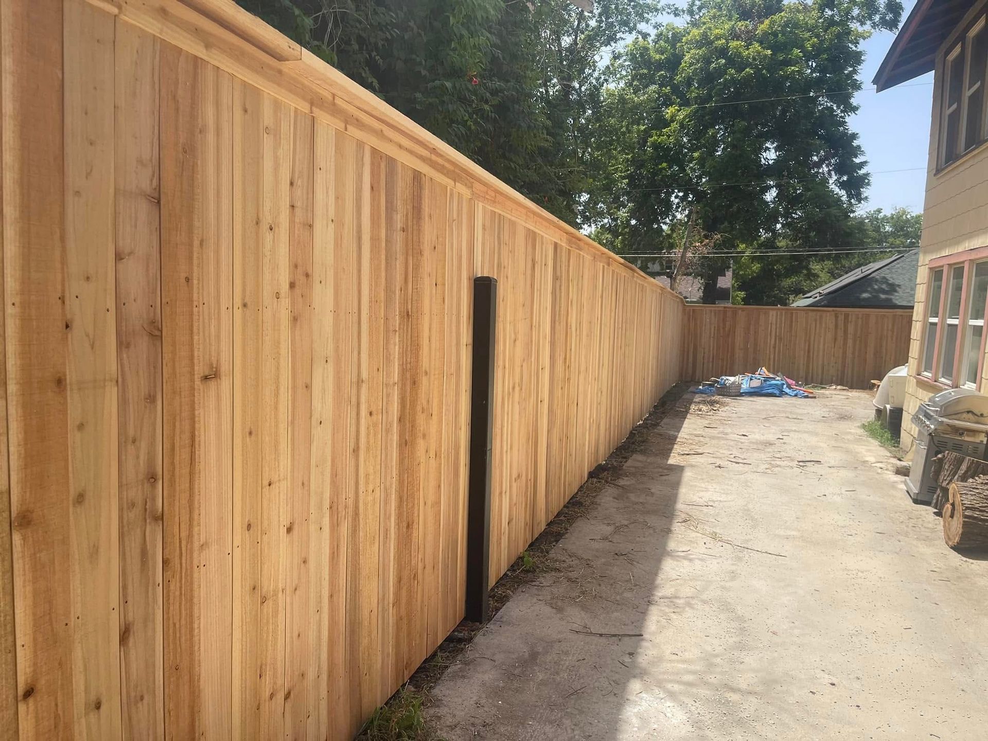 A new wooden privacy fence running along a concrete driveway next to a house under a clear blue sky.