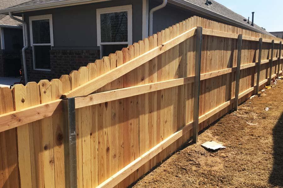 New wooden privacy fence with metal posts and horizontal rails installed beside a house on a sunny day.