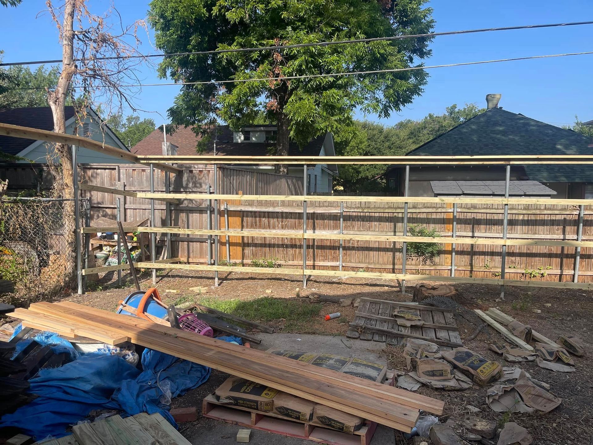 A backyard under construction featuring a tiered wooden shelf structure installed along a chain-link fence.