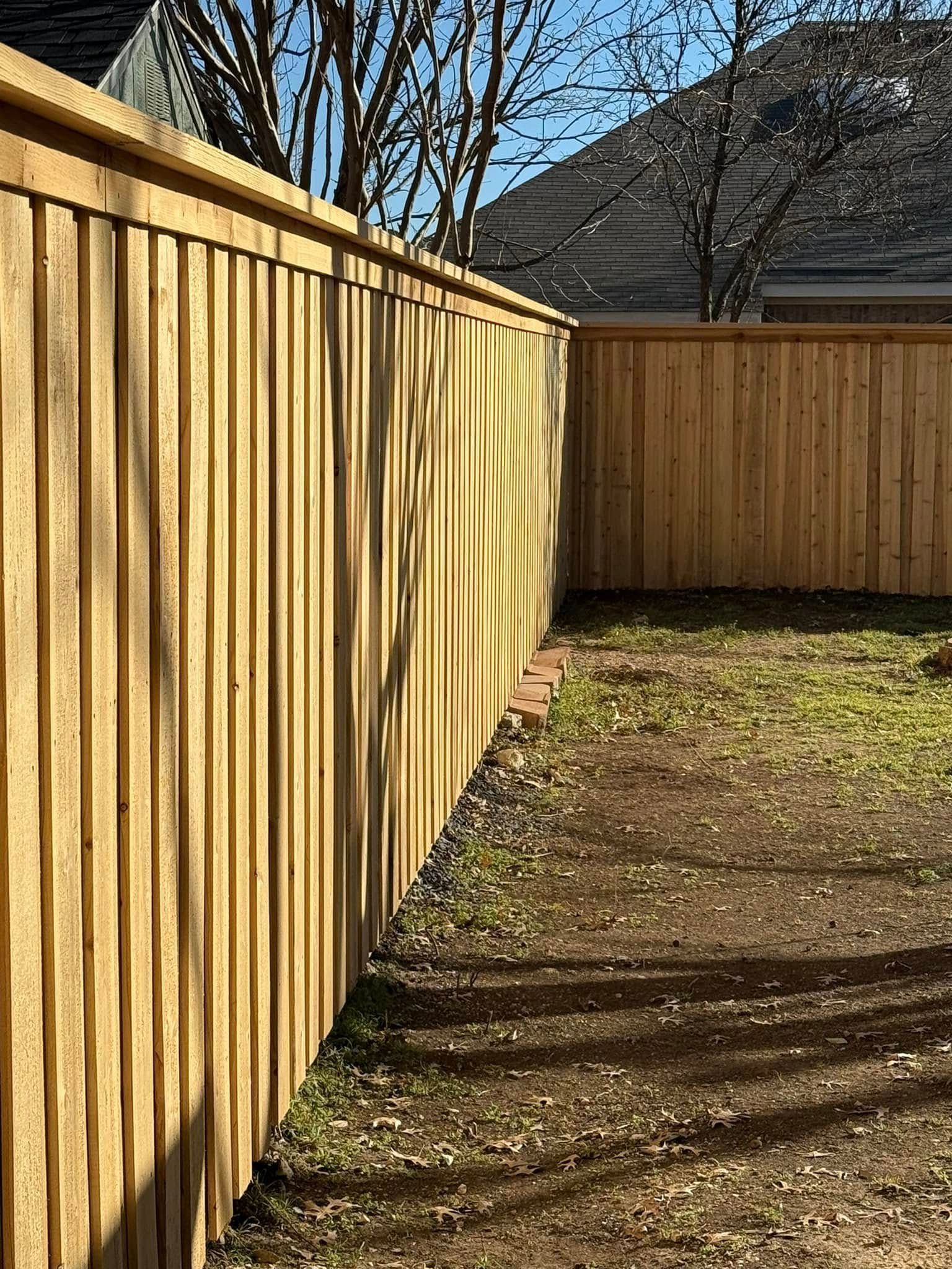 A perspective view of a new wooden privacy fence in a backyard during a sunny day.