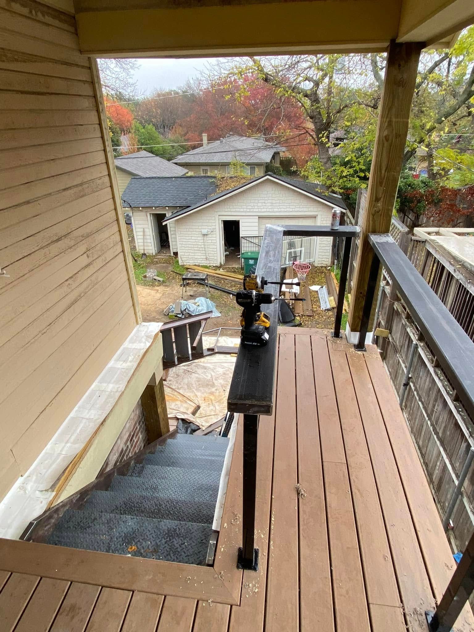 An outdoor wooden deck staircase viewed from above, overlooking a backyard with a garage, trees, and autumn foliage.