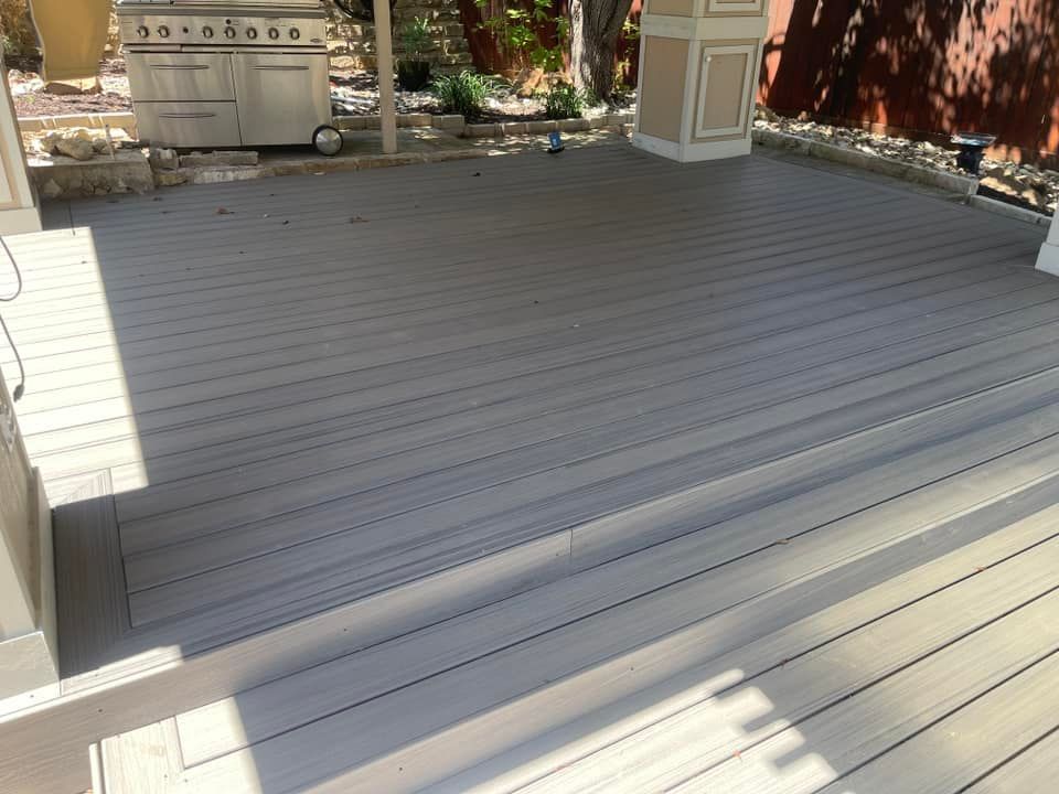 A modern gray composite deck with a single step leading to an upper level, featuring a stainless steel grill in the rear.