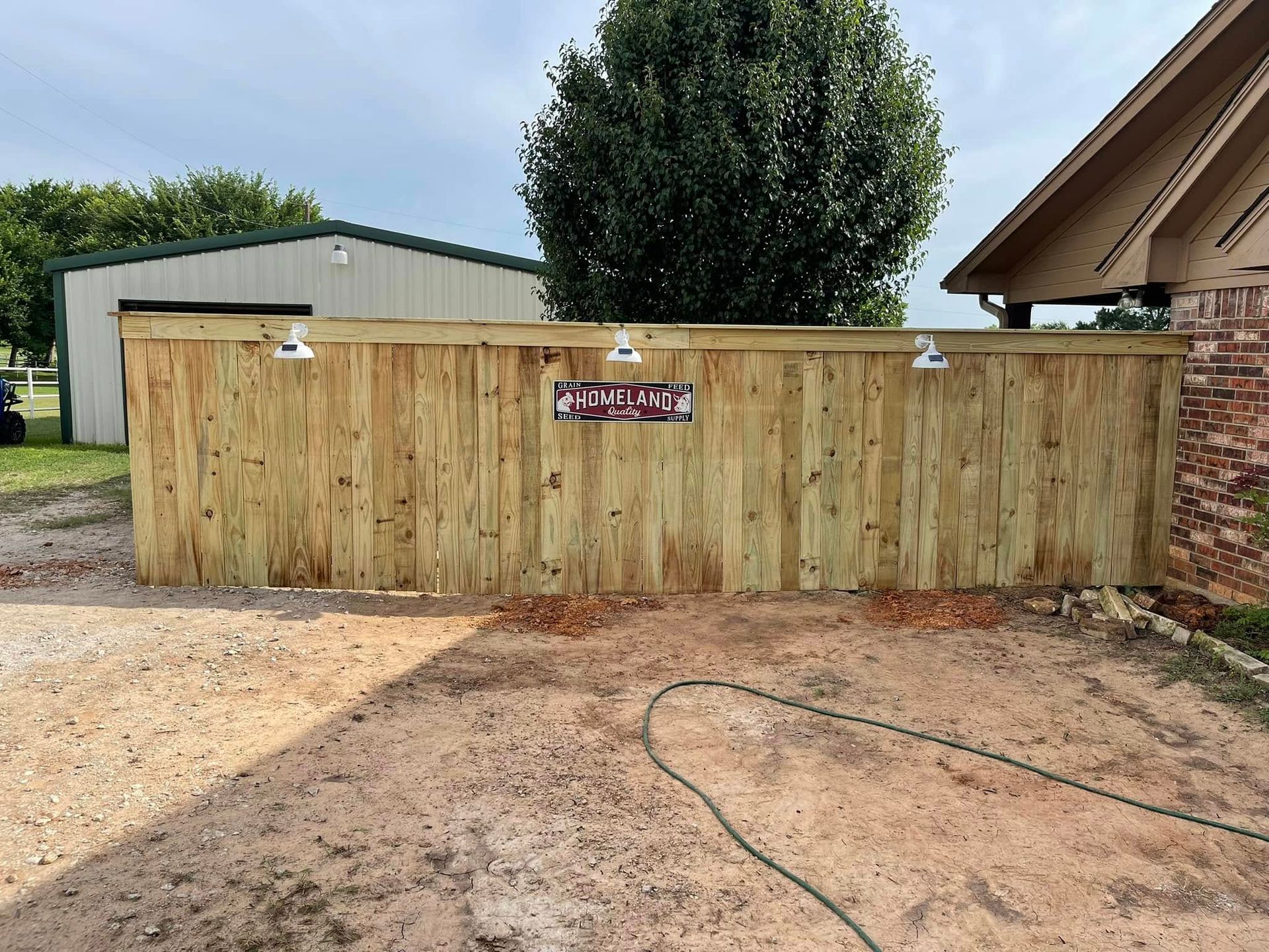 A newly installed wooden fence featuring three wall-mounted lights and a small rectangular sign centered on the boards.