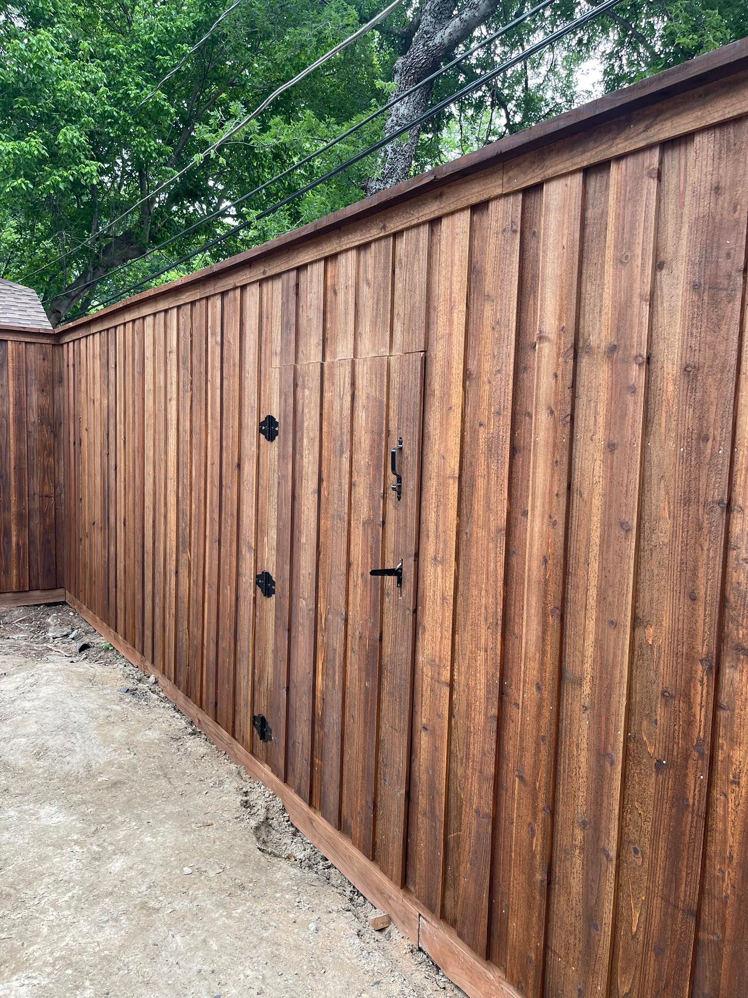 A brown wooden board-on-board fence with a matching gate featuring black metal hinges and a latch.