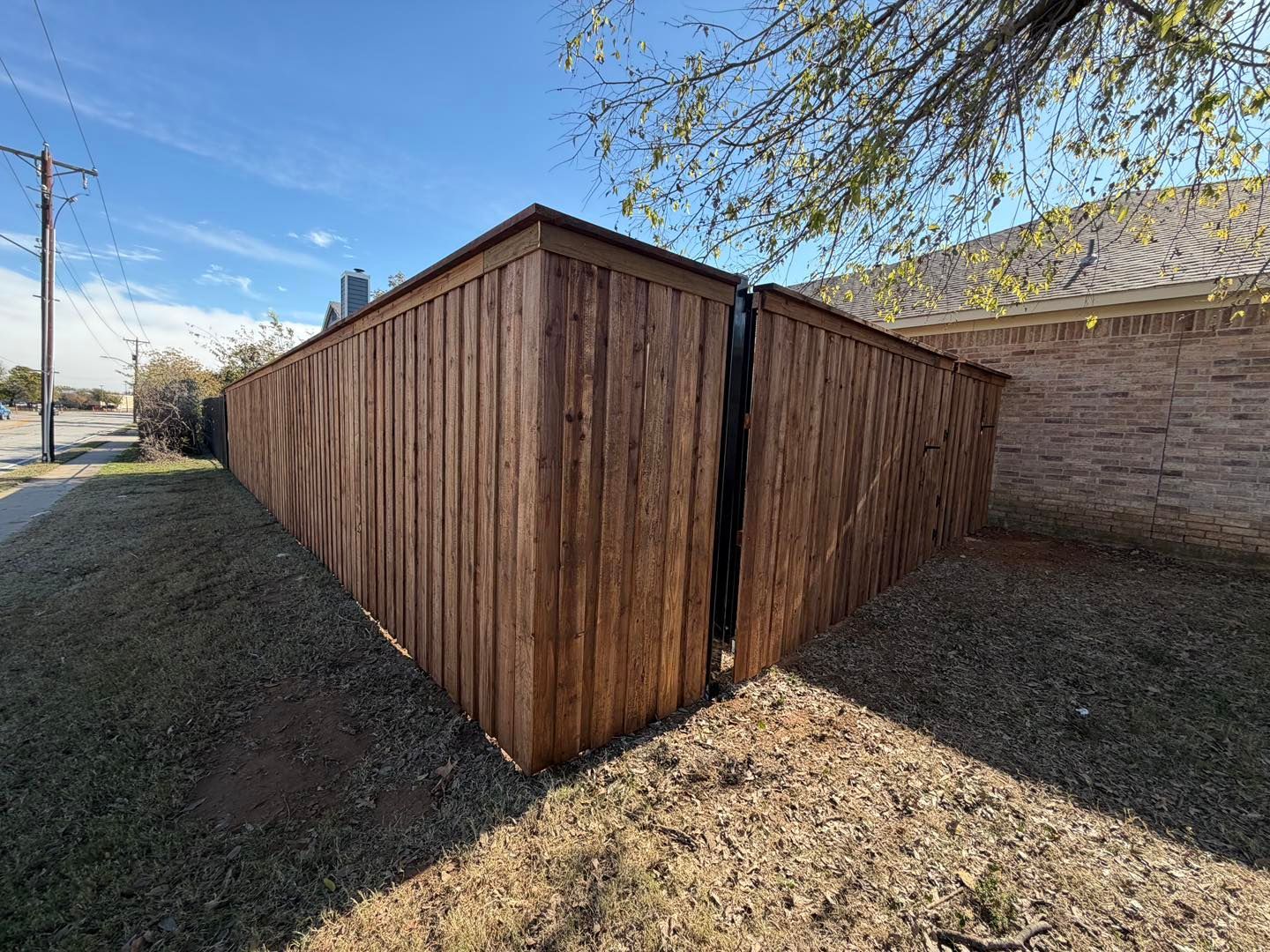 A tall wooden fence corner in a residential yard with a vertical gap between the fence panels.