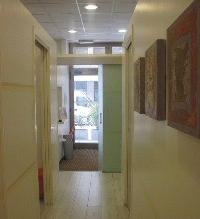Stretto corridoio d'ufficio con quadri incorniciati su pareti beige e una porta luminosa in fondo.