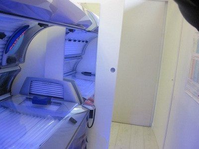 Interno di una cabina abbronzante illuminata di blu con porta bianca aperta in una piccola stanza