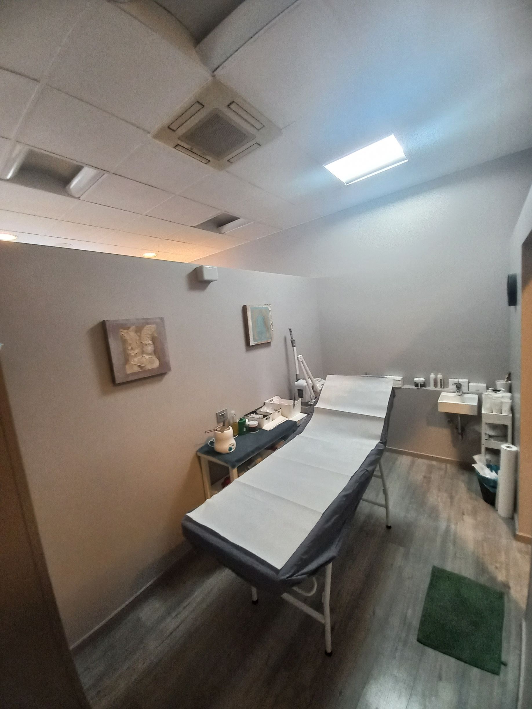 Sala visite della clinica con lettino da visita, luci a soffitto, quadri alle pareti e armadietti sulla destra.