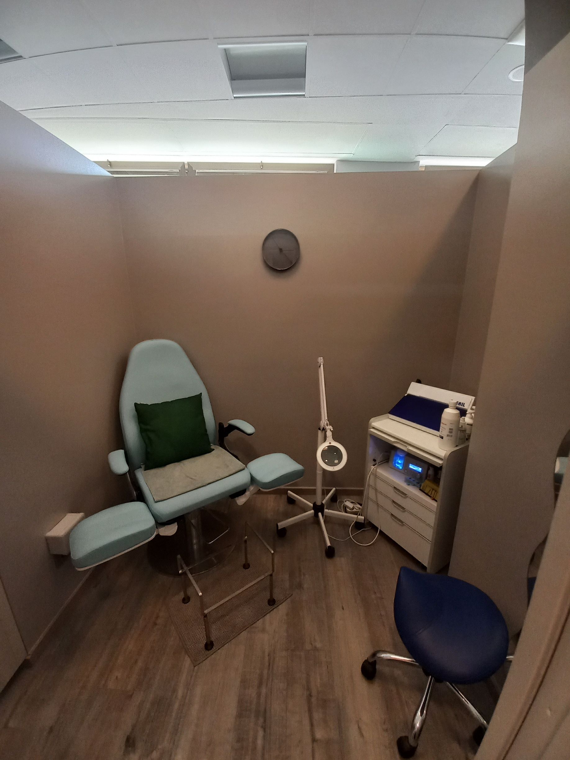 Piccola sala visite in ambulatorio con sedia medica, sgabello e attrezzature, su pareti color beige.