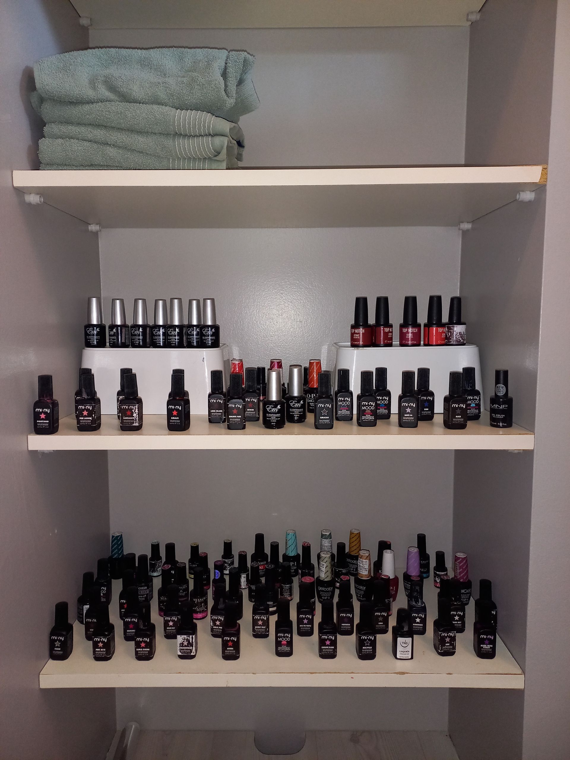 Ripiani con asciugamani impilati e file di boccette di smalto su due ripiani